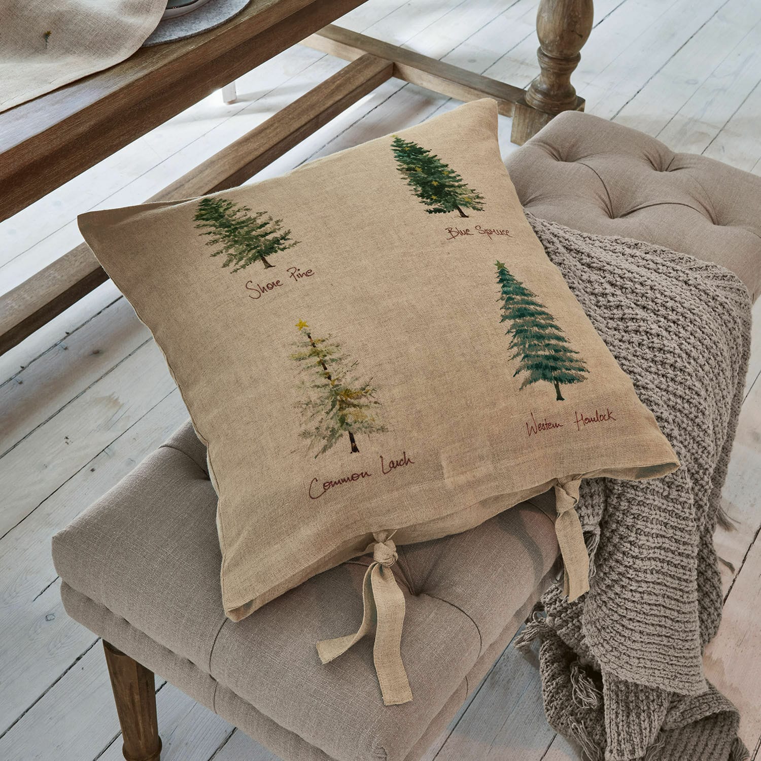Funda de cojín Jarrier Cojín beige de lino con estampado de árboles y lazos atados sobre asiento gris