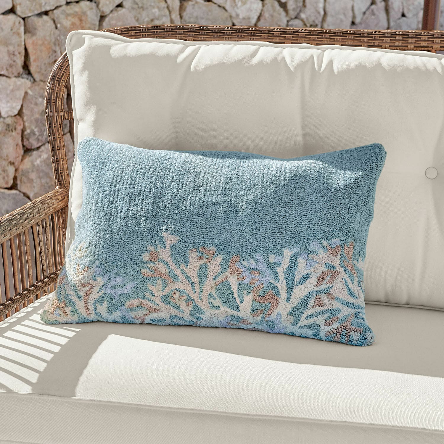 Funda de cojín para interior y exterior Dorlancourt Cojín decorativo azul de material suave con diseño de coral sobre sofá claro de ratán.