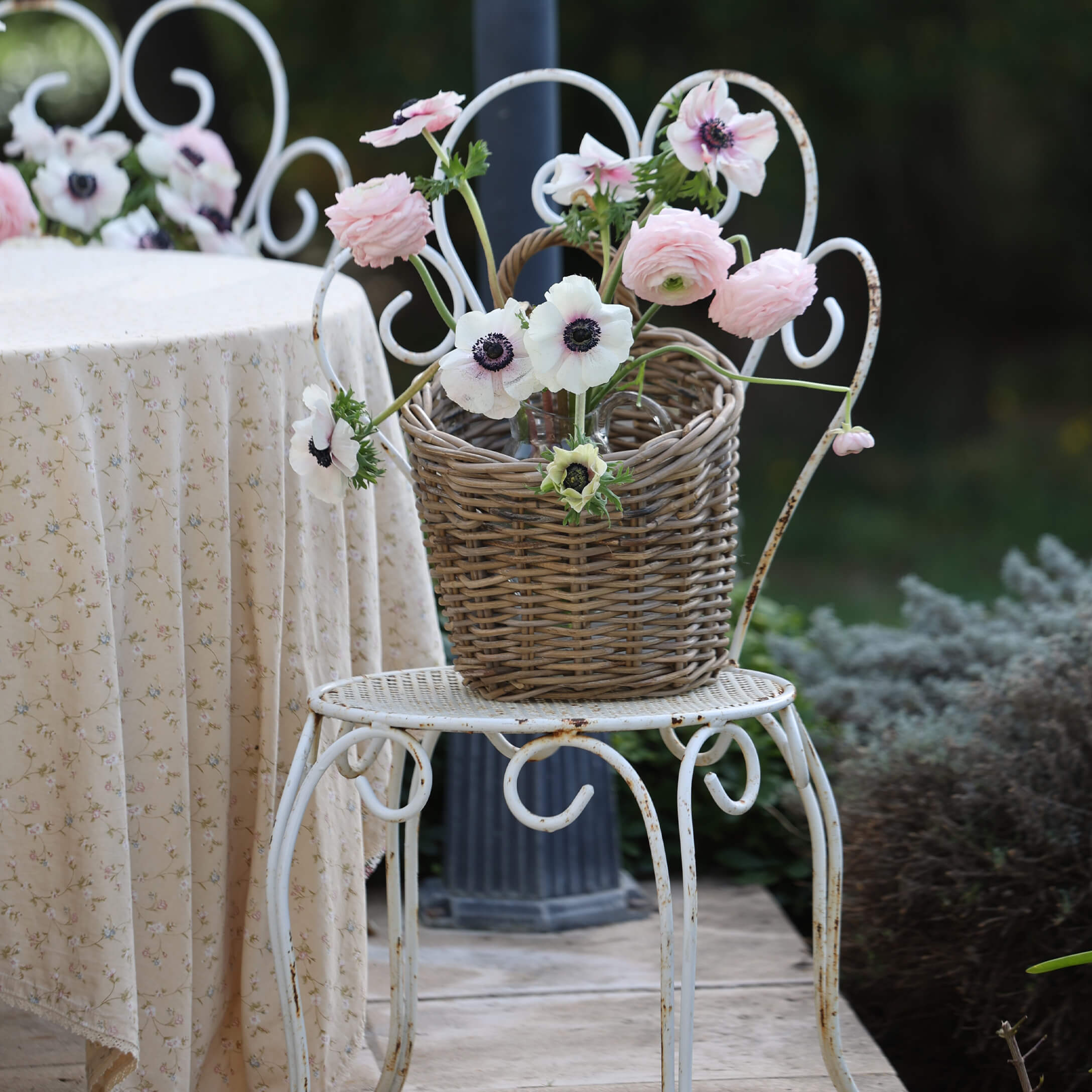 Cesta de mimbre con flores rosas y blancas sobre silla metálica blanca en jardín