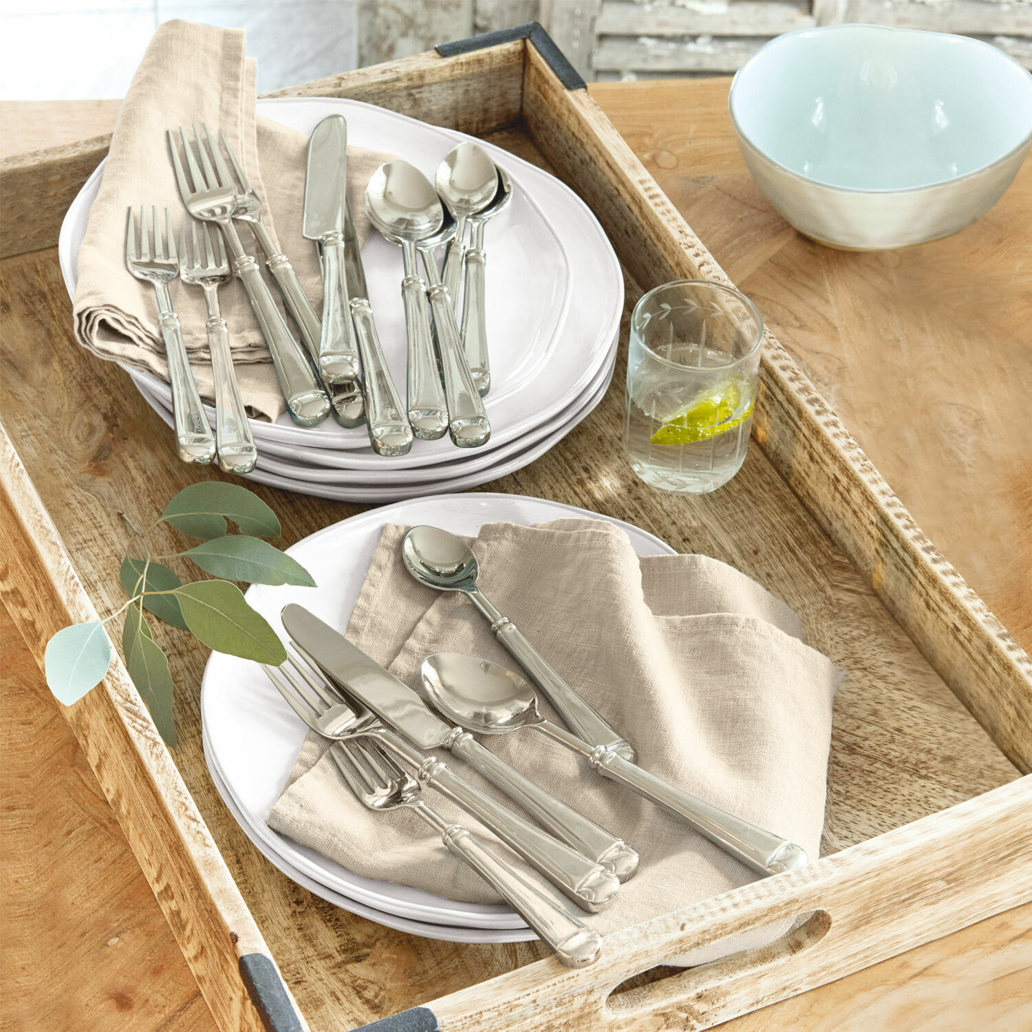 Cubiertos Eriat Juego de cubiertos plateados sobre platos blancos con servilletas beige en bandeja de madera