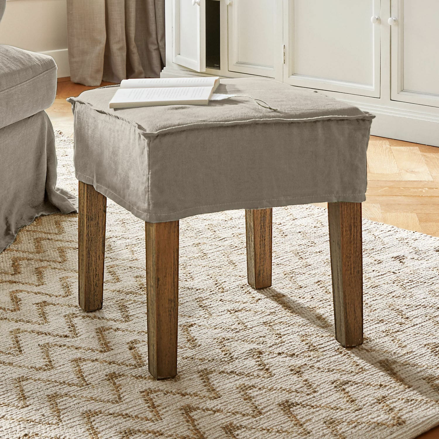 Taburete Vionnique Puf beige con funda de algodón y patas de madera sobre alfombra clara en sala de estar