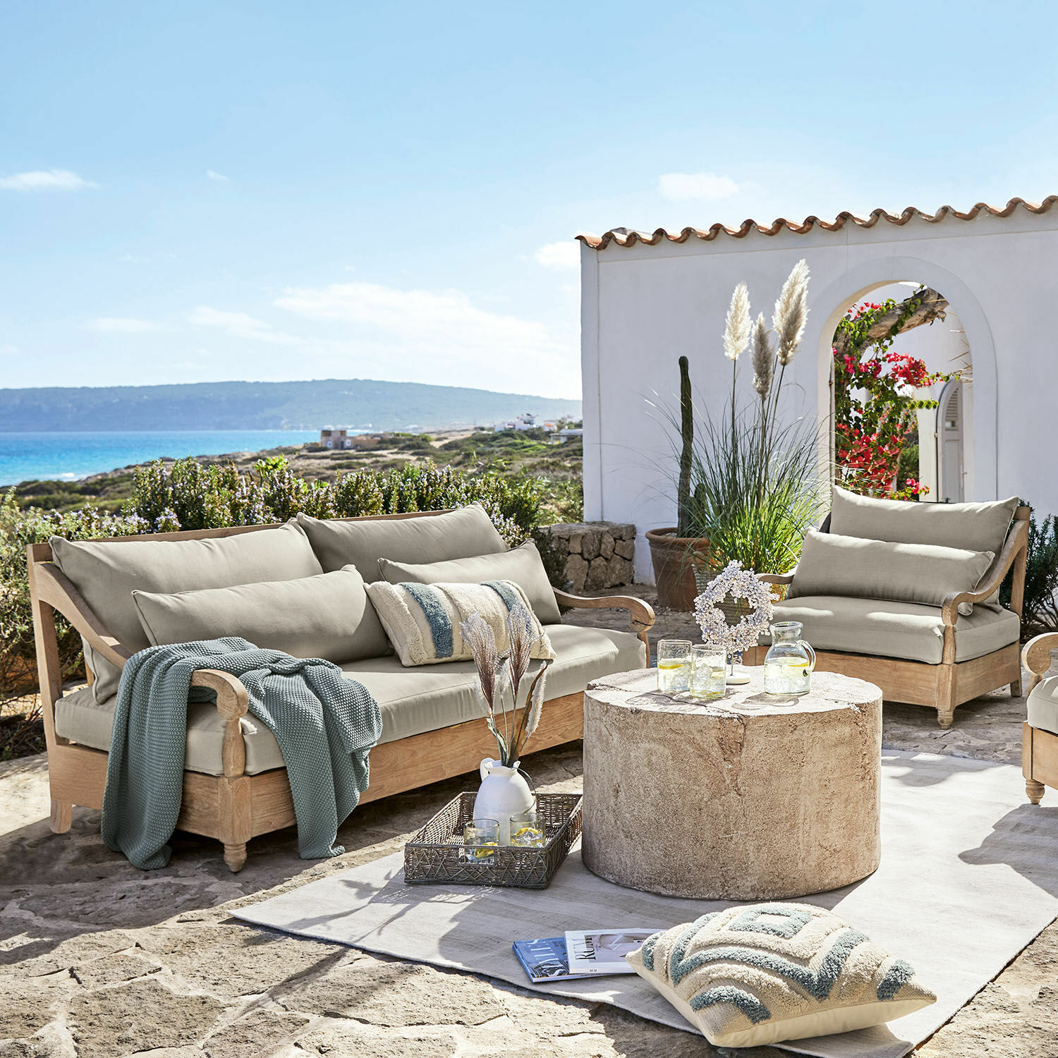 Grupo de asientos Montcassin Conjunto de muebles de jardín de madera clara con cojines beige en terraza de piedra con vista al mar