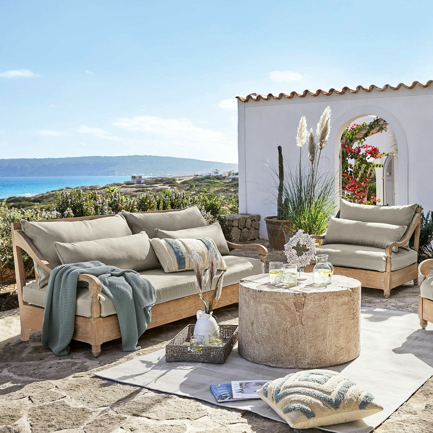 Grupo de asientos Montcassin Conjunto de muebles de jardín de madera clara con cojines beige en terraza de piedra con vista al mar
