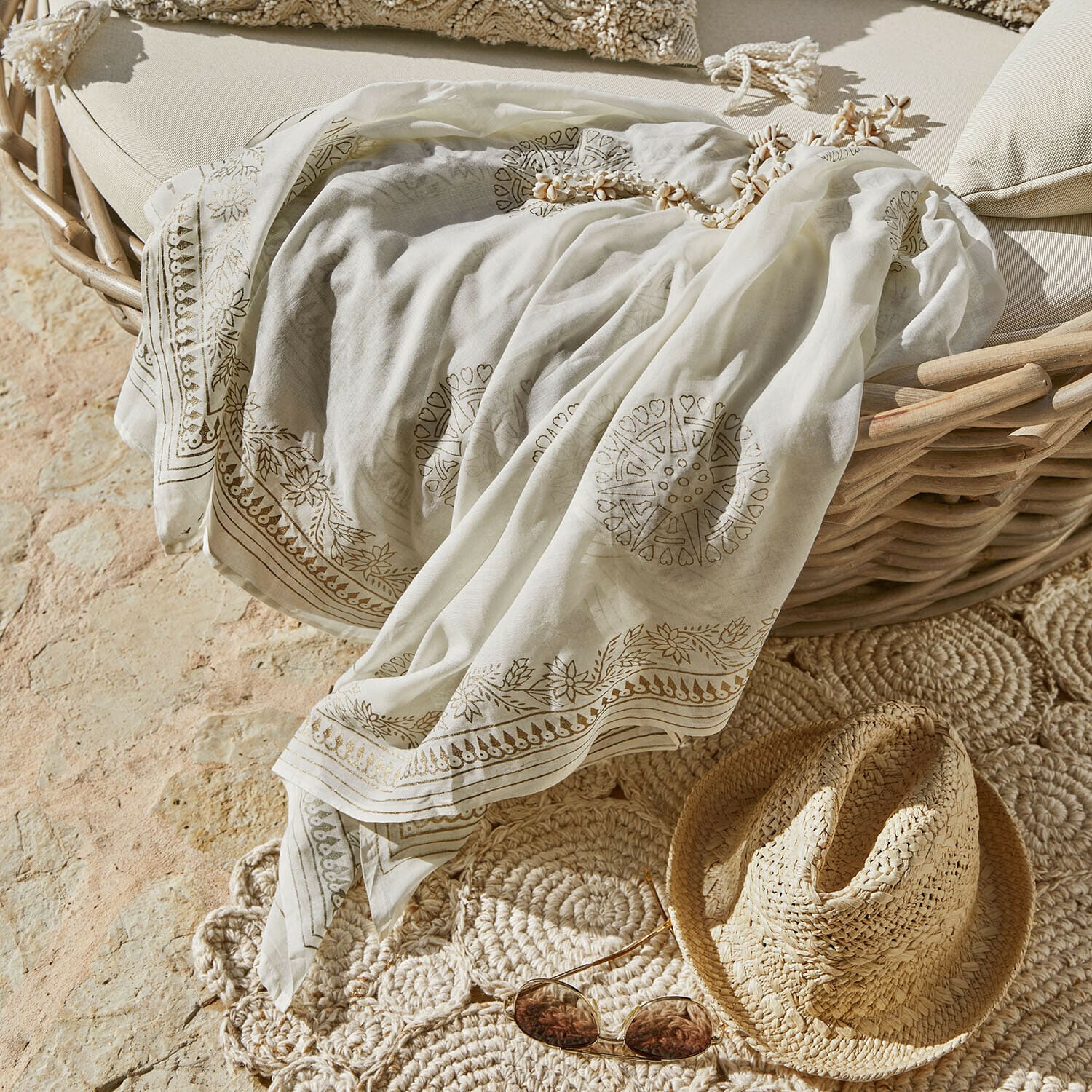Chal Lamérise Pañuelo blanco ligero con diseño delicado sobre sillón de mimbre junto a sombrero de paja y gafas de sol