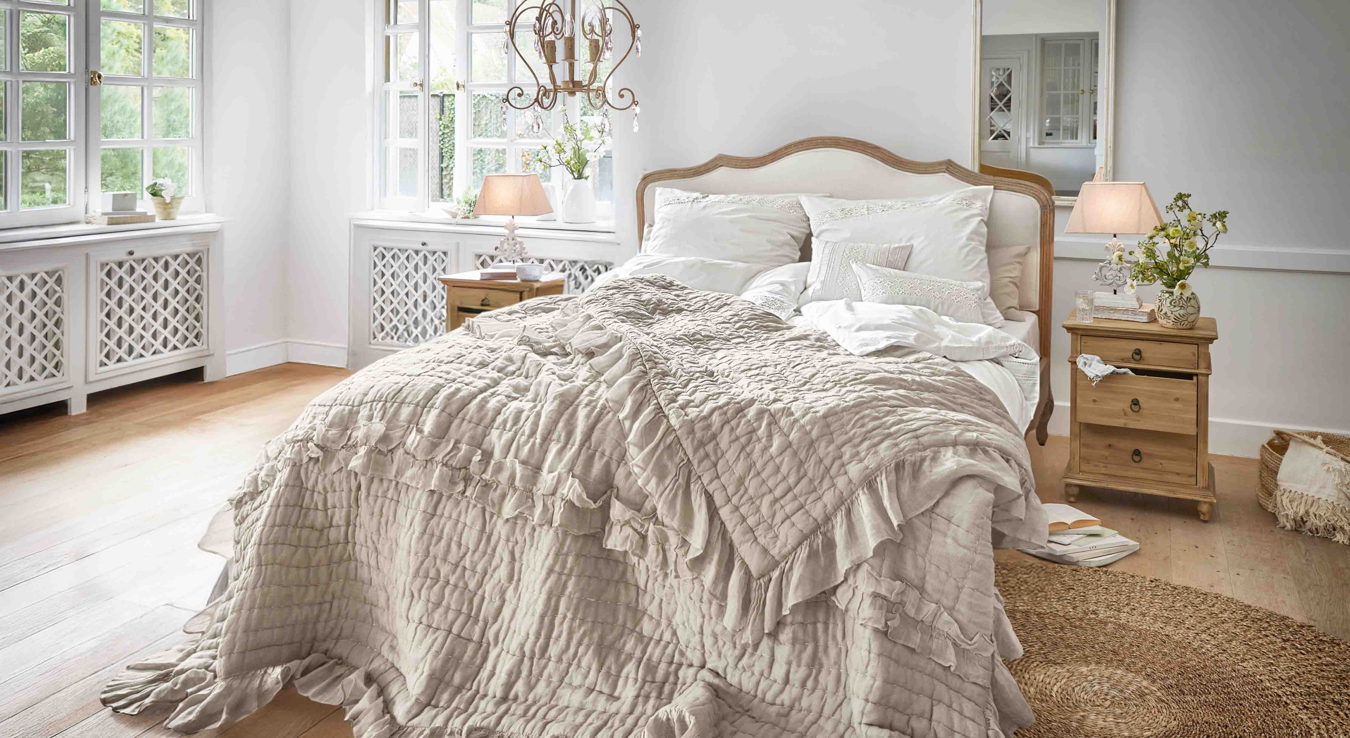 Dormitorio acogedor con cama con colcha beige con volantes y mesitas de noche de madera clara