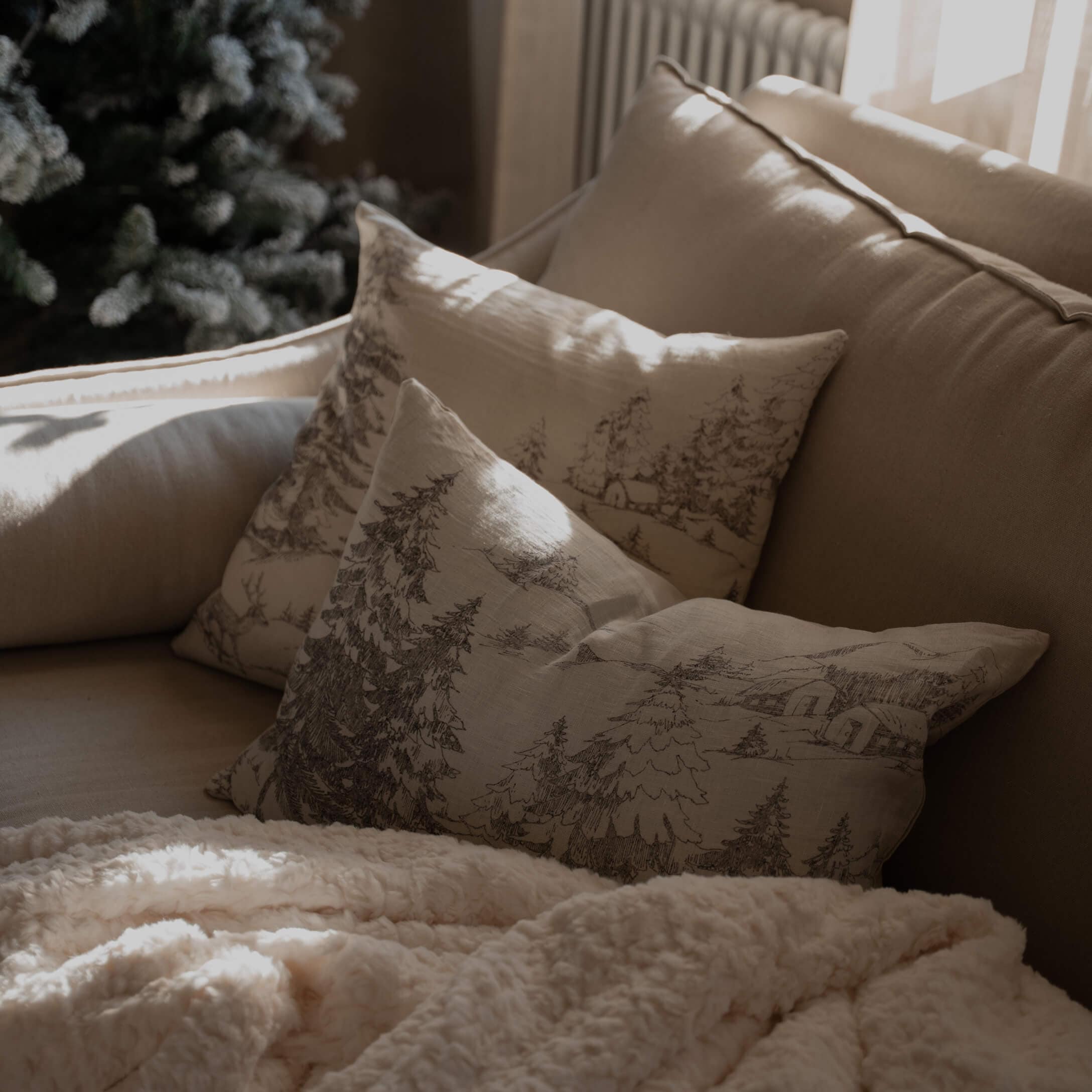 Sofá beige con cojines estampados de bosque y manta cremosa suave para salón acogedor