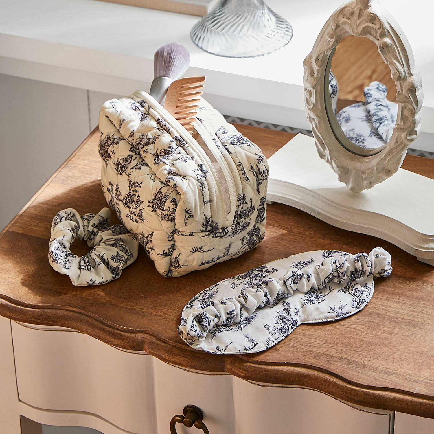 Set para dormir Felencio Neceser acolchado beige con estampado negro, diadema y antifaz sobre mesa de madera, accesorios de cuidado personal