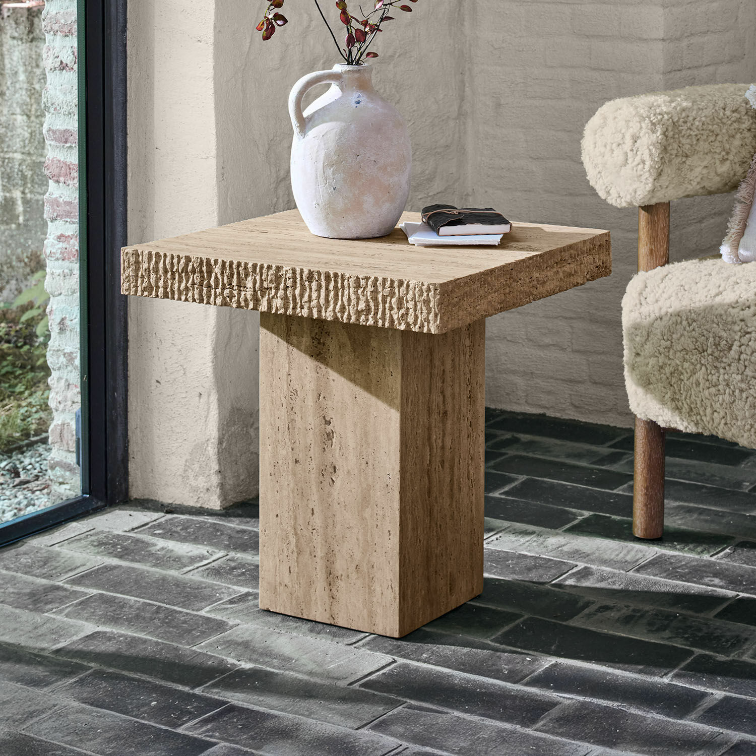 Mesa auxiliar Gainsbury Mesa auxiliar cuadrada de travertino beige sobre suelo oscuro de ladrillo