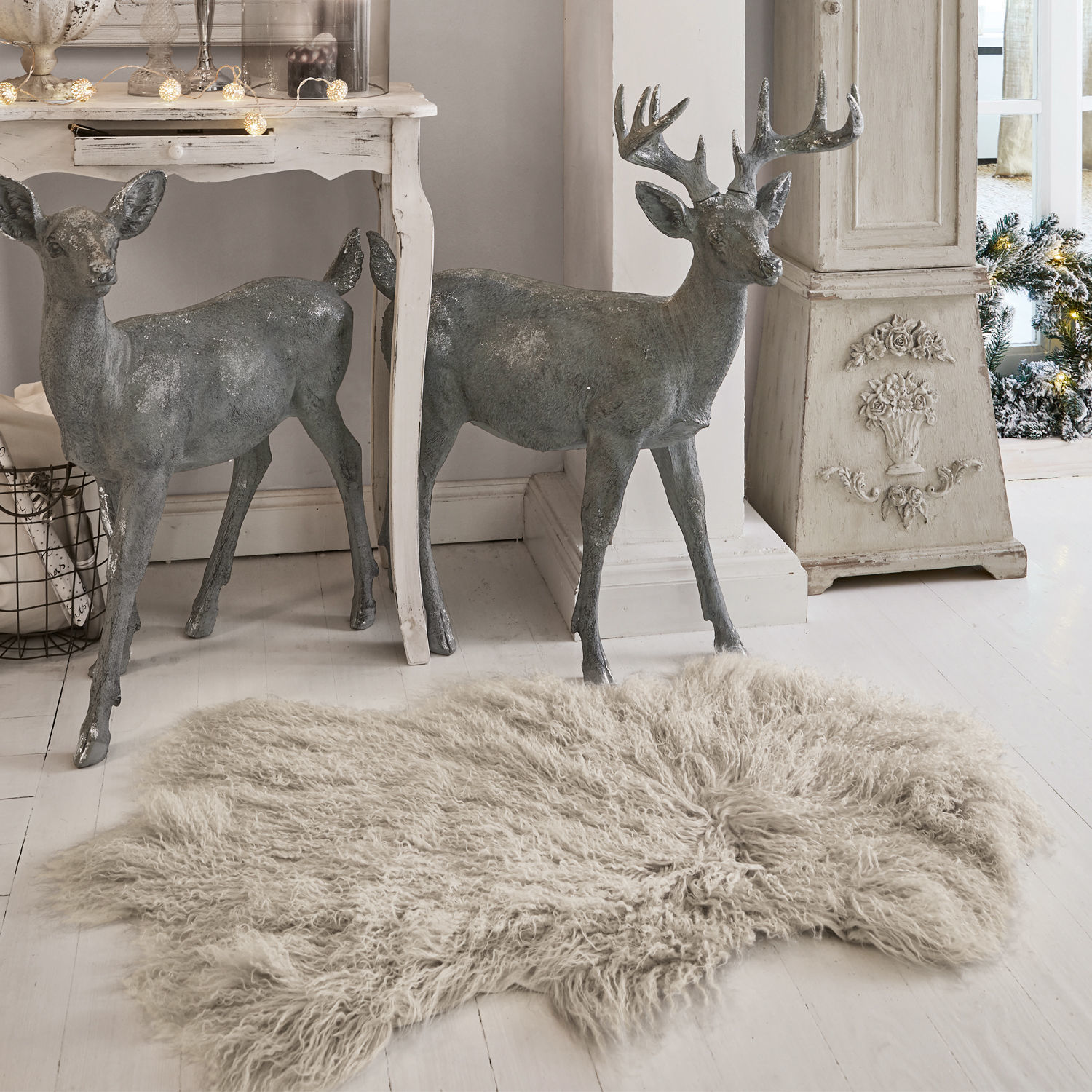 Piel de cordero Gad Figuras decorativas de ciervos grises de metal junto a mesa blanca y alfombra beige de pelo largo