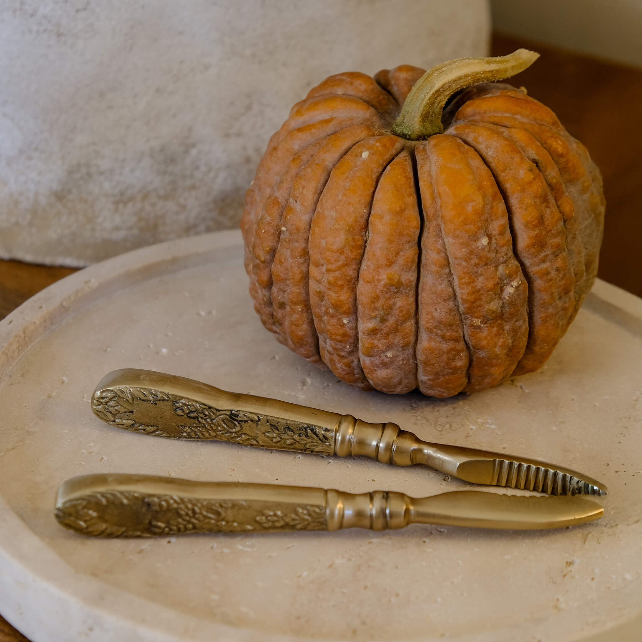 Juego de cuchillos de latón con mangos decorativos sobre bandeja beige junto a calabaza naranja