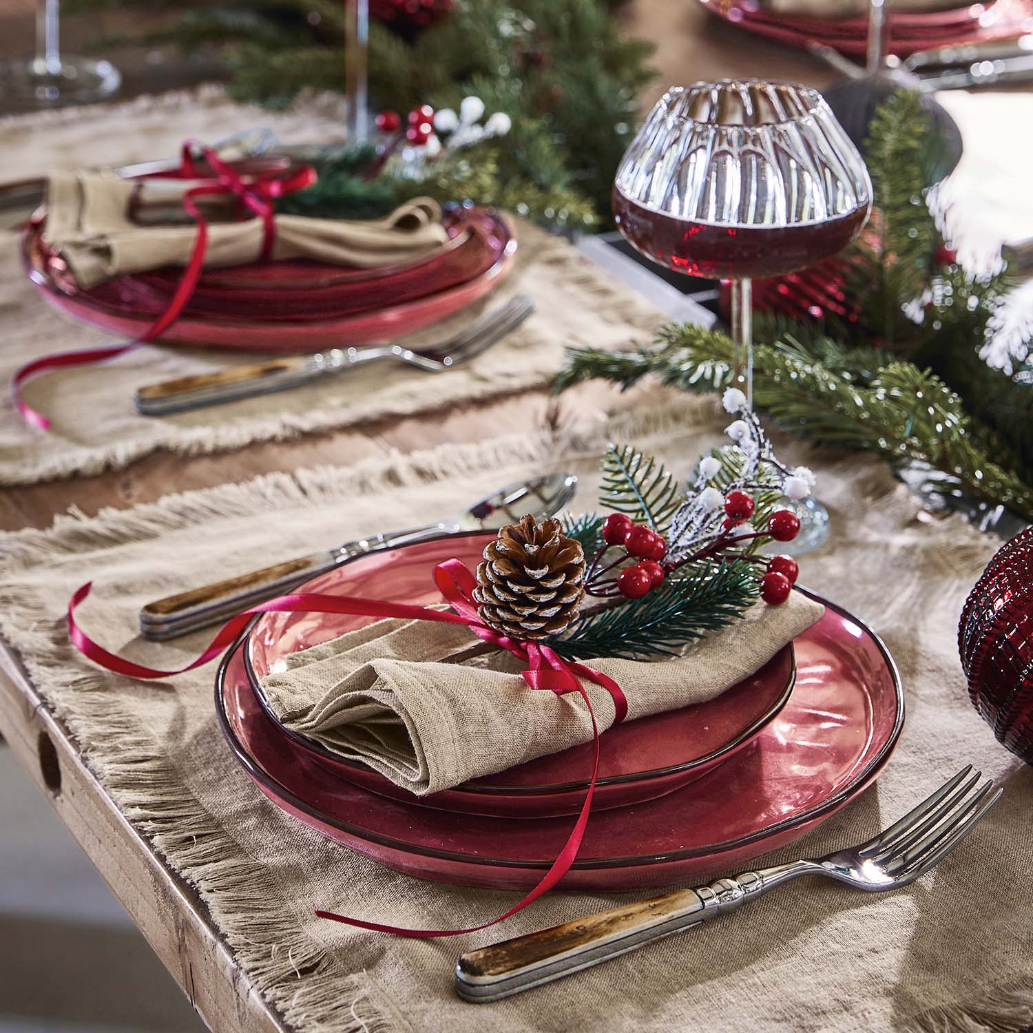 Mesa decorada para Navidad con platos de cristal rojo y adorno de piña y bayas rojas