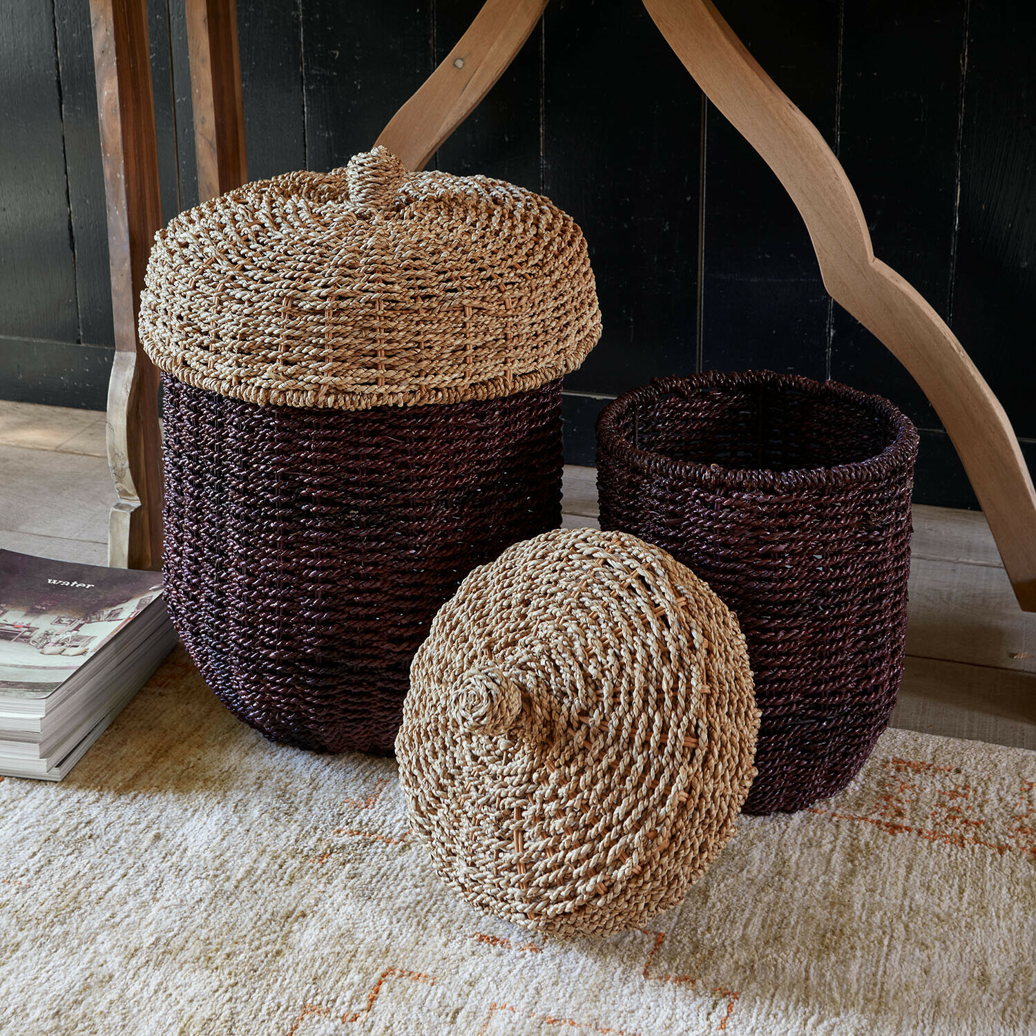Set de 2 cestas Aelwyn Conjunto de dos cestas marrones con tapas de material trenzado natural sobre alfombra