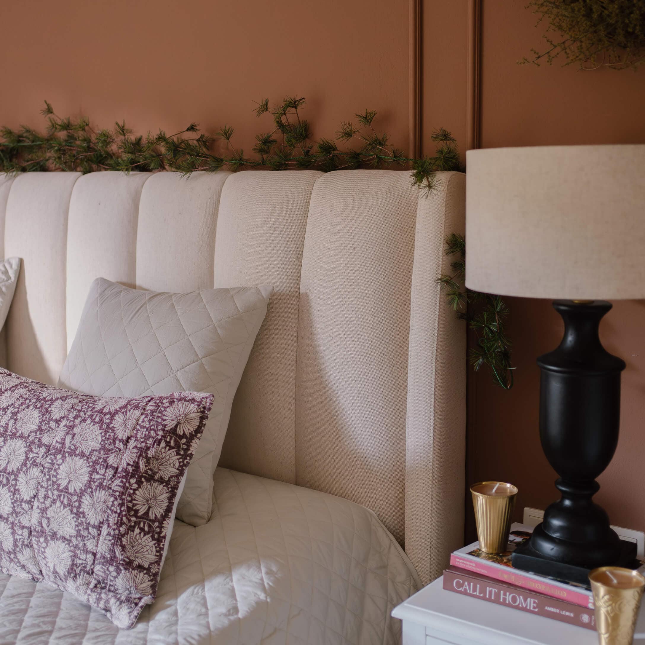 Cabecero tapizado beige con cojines y lámpara sobre mesita de noche en habitación acogedora