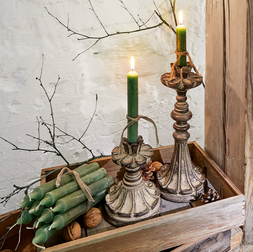 Dos candelabros decorativos con velas verdes sobre bandeja de madera con nueces y ramas