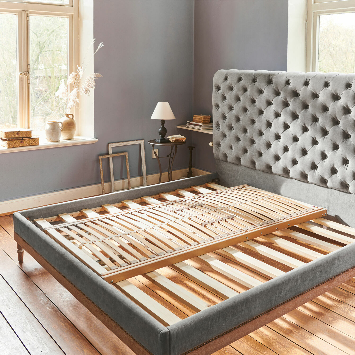 Somier Yount Cama tapizada gris con cabecero capitoné y base de madera en habitación luminosa