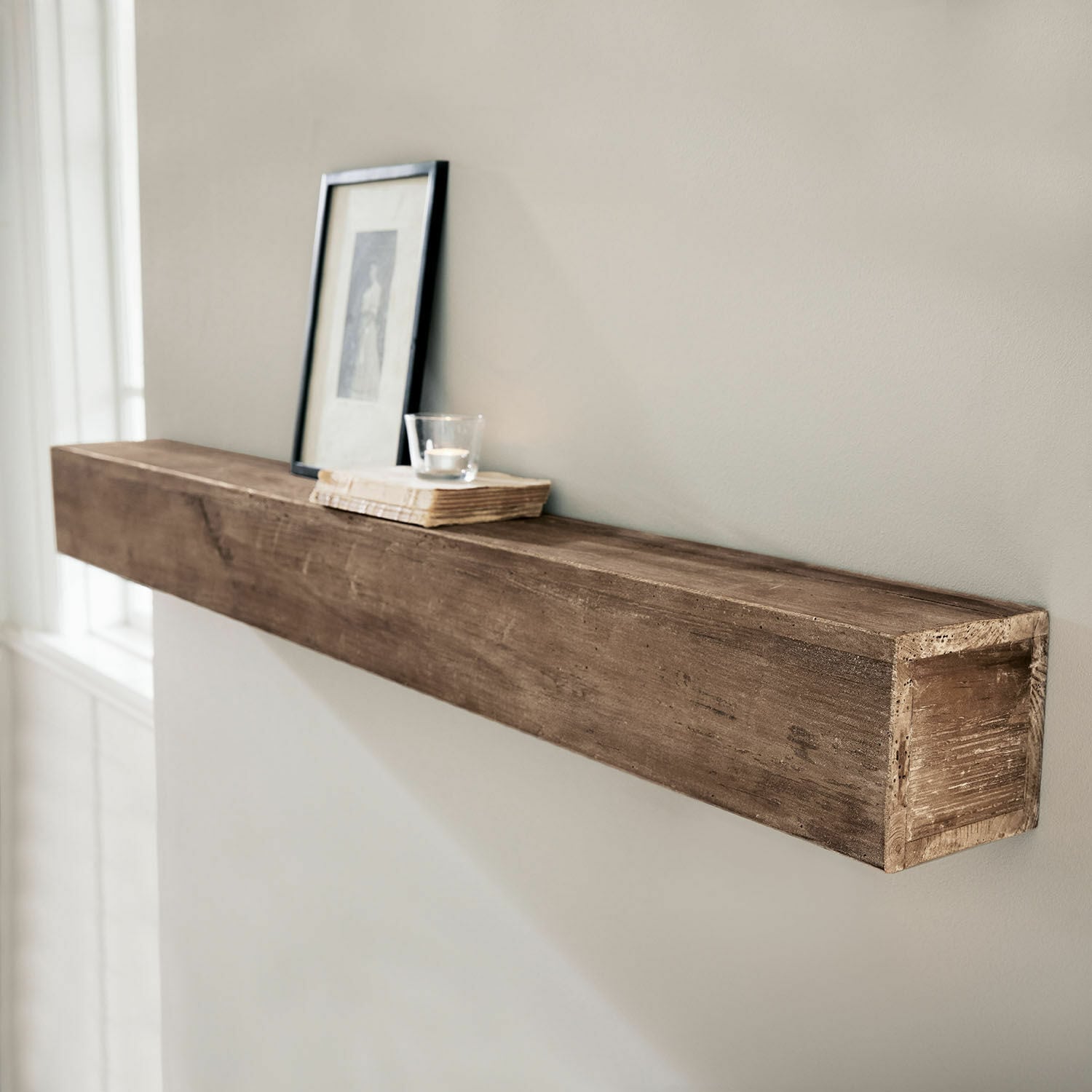 Estante de pared Visayas Estante de pared de madera marrón con marco decorativo y vela sobre un libro