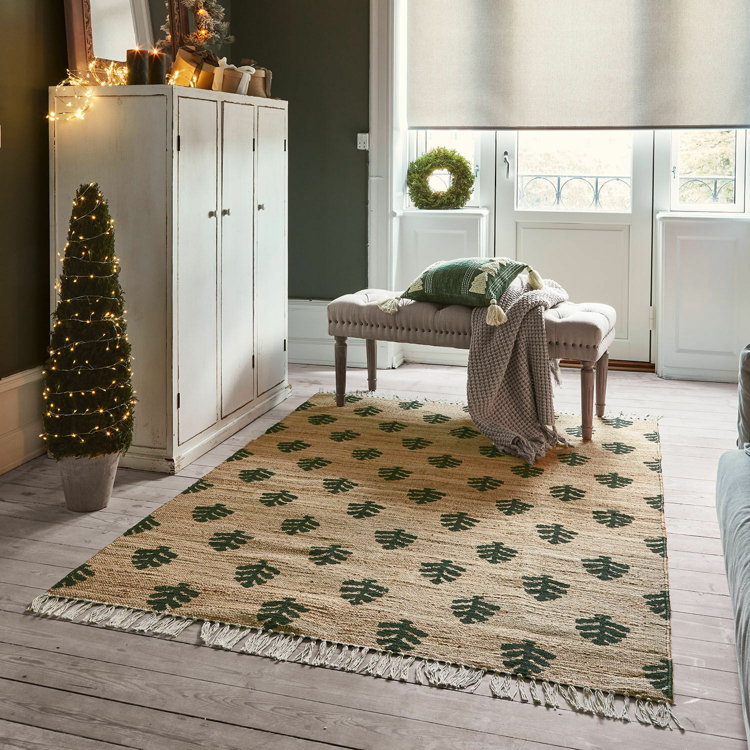 Alfombra beige con patrón de hojas verdes y flecos sobre suelo de madera clara en sala luminosa