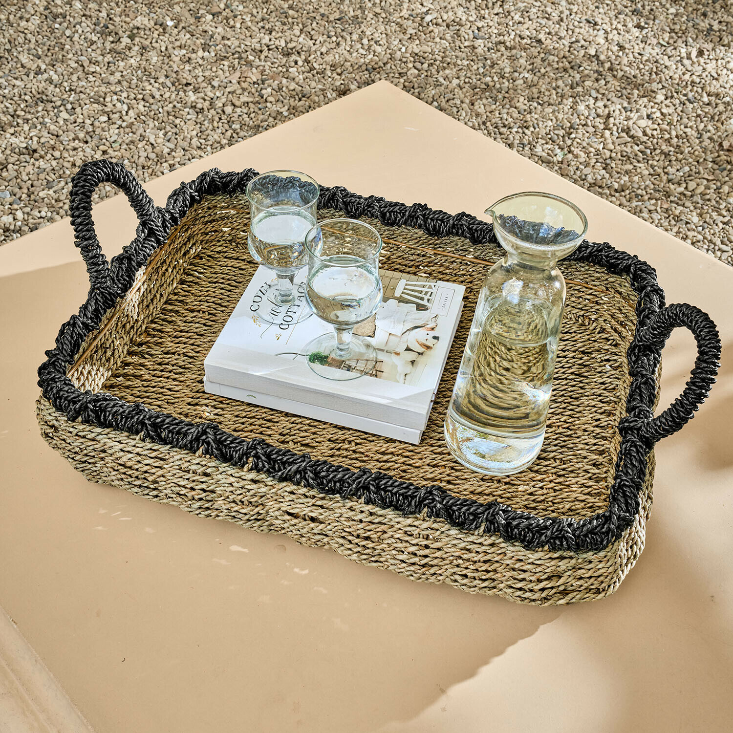 Bandeja Tarevo Bandeja rectangular de hierba marina trenzada con borde negro y asas, con jarra y vasos sobre mesa