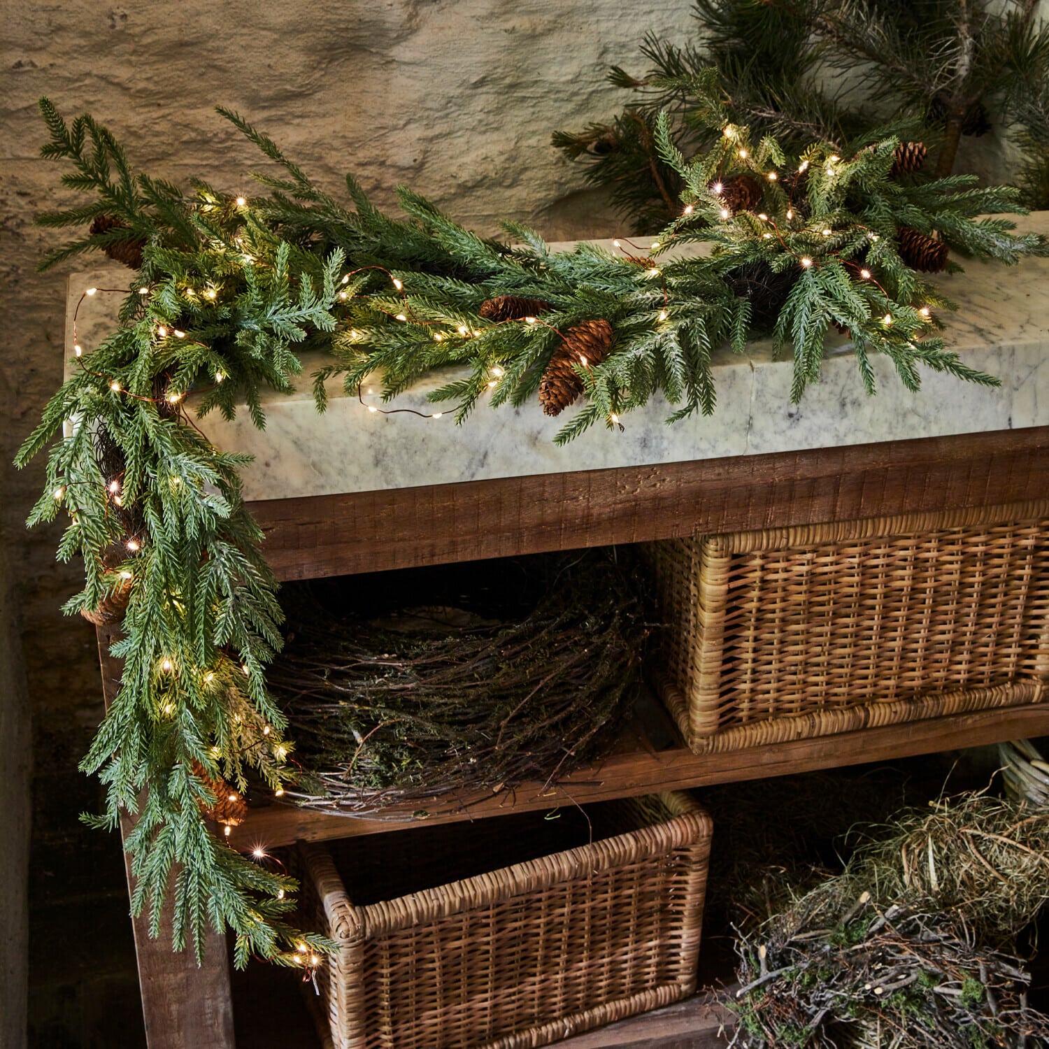 Guirnalda LED Sahani Corona decorativa de ramas verdes y piñas con luces LED sobre mesa de madera