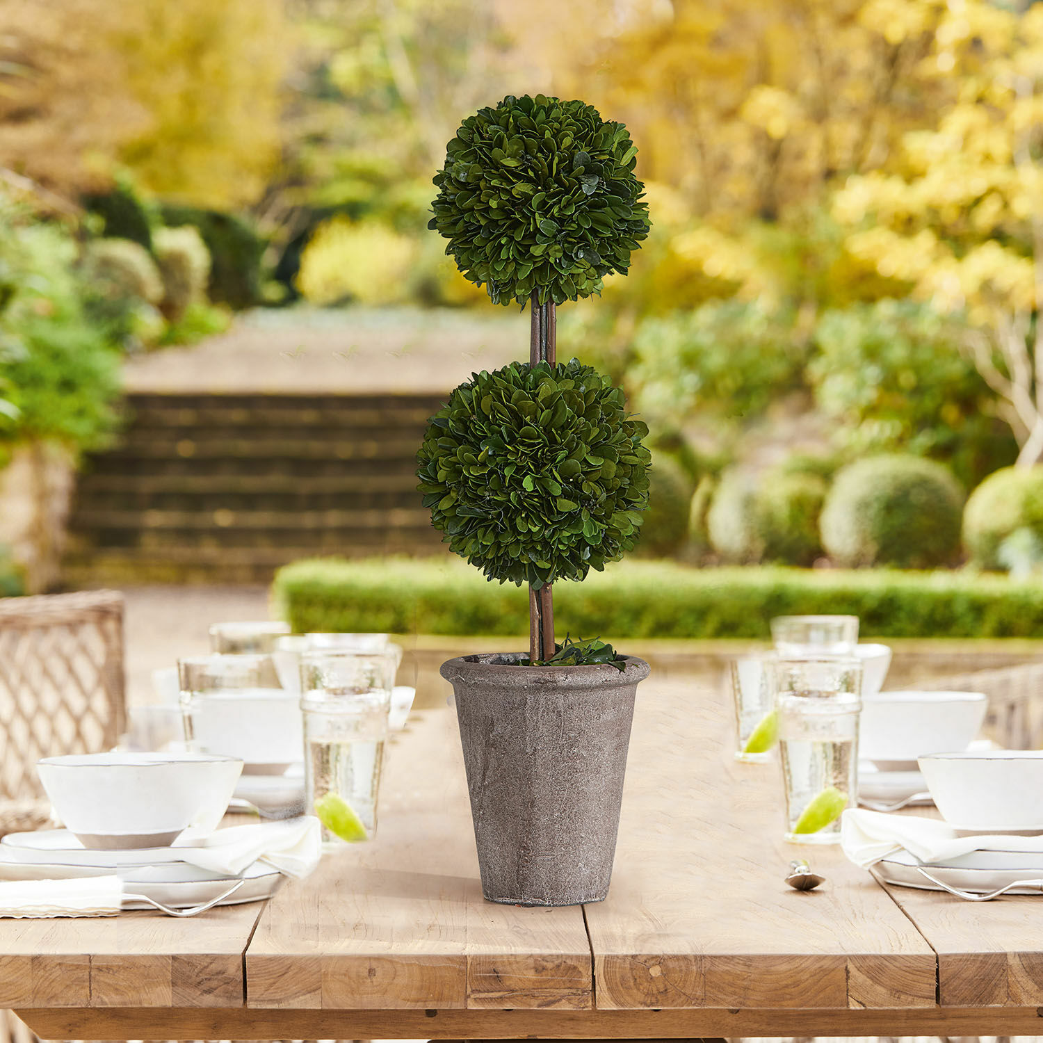 Árbol decorativo Noisse Planta decorativa artificial en maceta de piedra gris sobre mesa de madera en jardín
