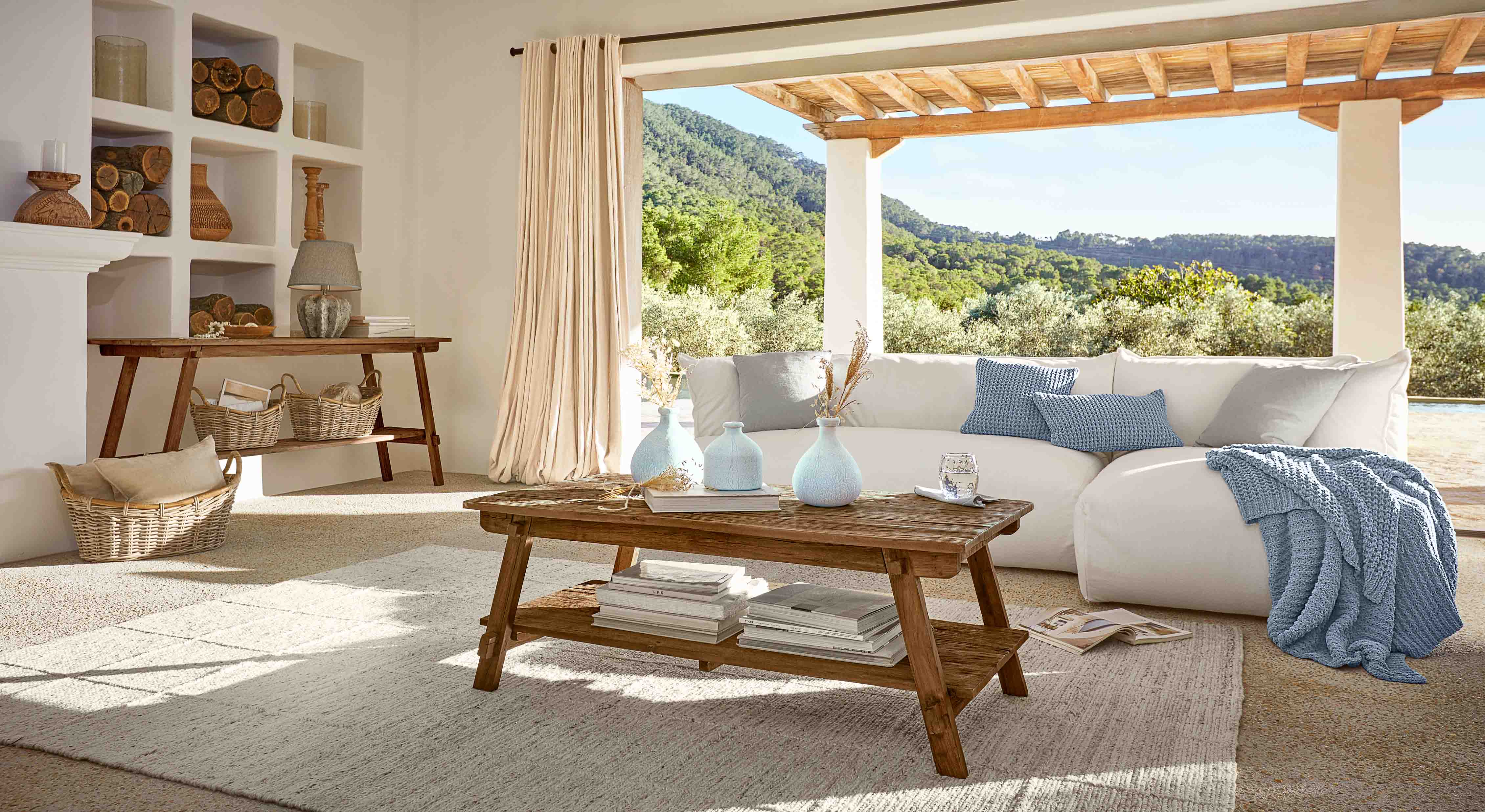 Sala acogedora con mesa de centro de madera y sofá blanco con manta y cojines azules