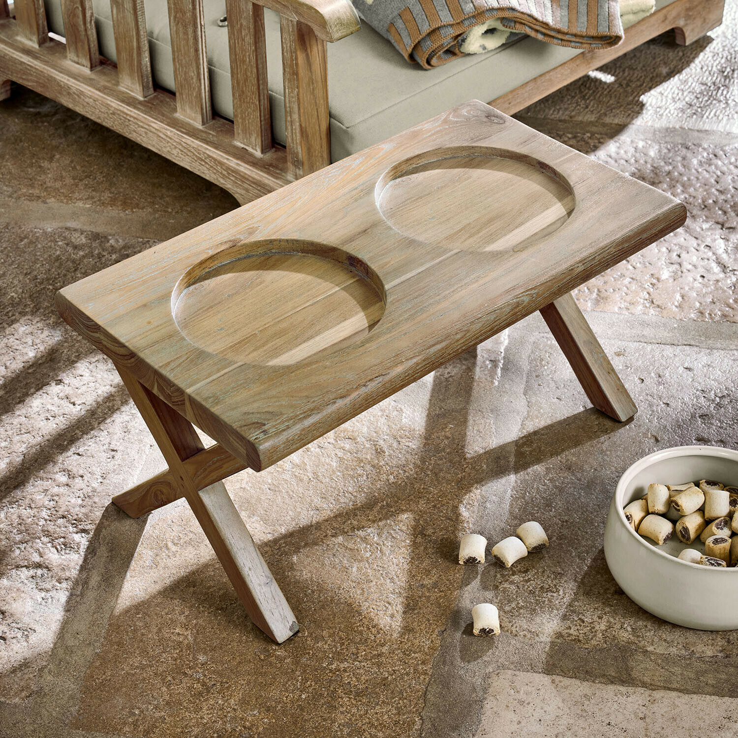 Soporte para comederos Felluna Mesa plegable de madera clara con dos huecos redondos junto a un sofá y un cuenco con snacks