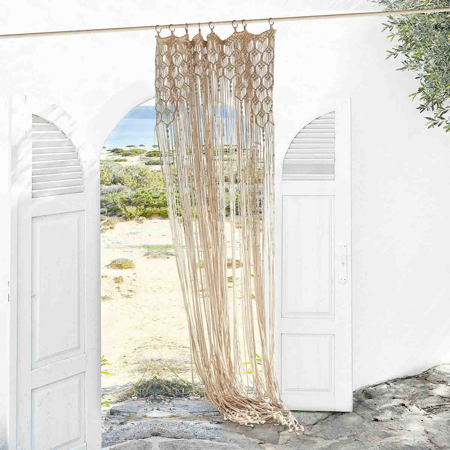 Cortina macramé beige de algodón colgada en entrada blanca, decoración interior y protección solar