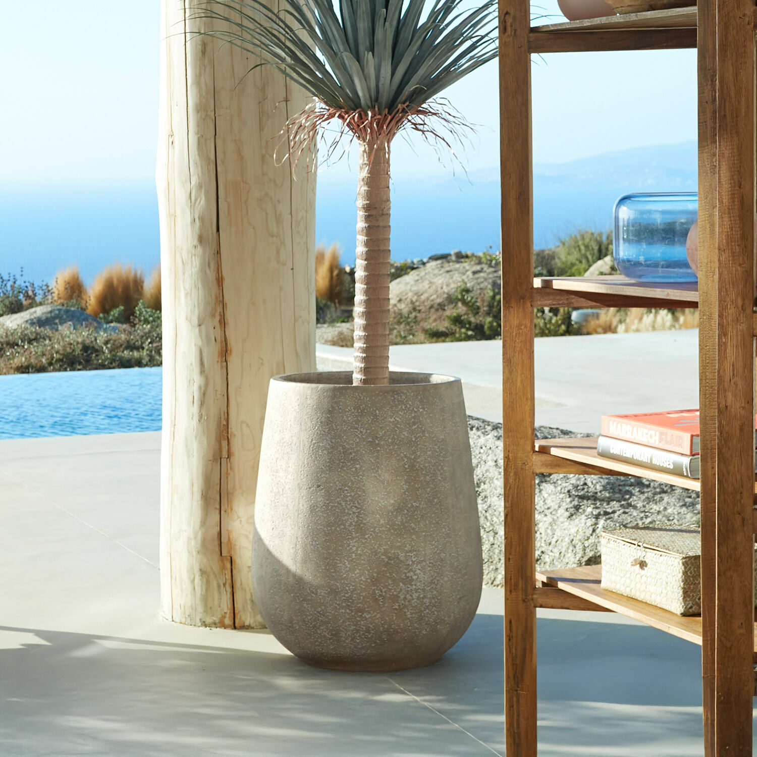 Jardinera Bressac Maceta grande de hormigón gris con planta decorativa en terraza con vista al mar