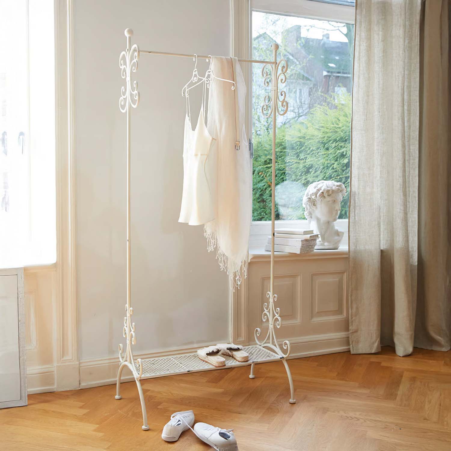 Perchero metálico blanco con detalles decorativos en habitación luminosa con suelo de madera