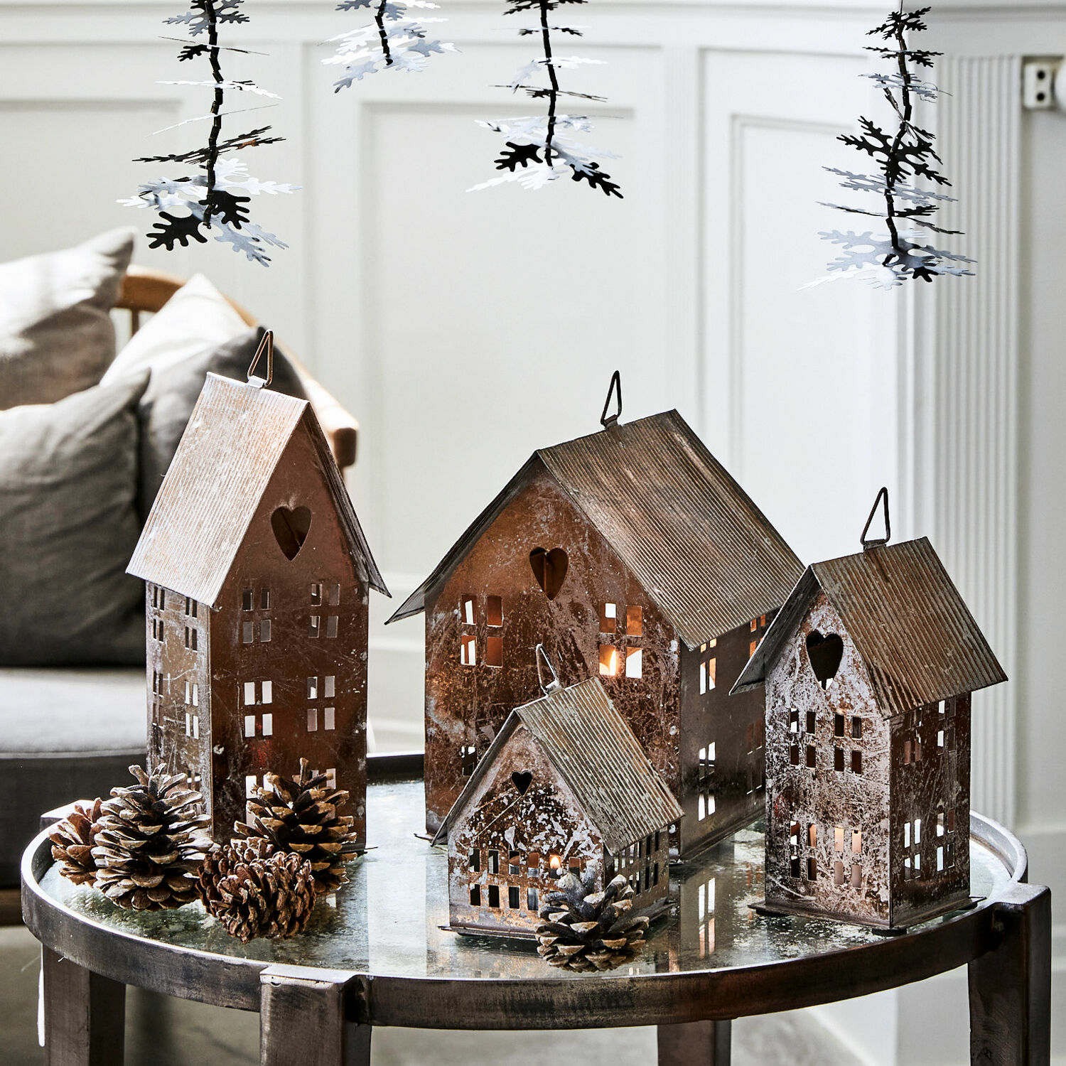 Set de 4 farolillos Treyford Faroles metálicos en forma de casas con ventanas en forma de corazón sobre mesa de cristal con piñas