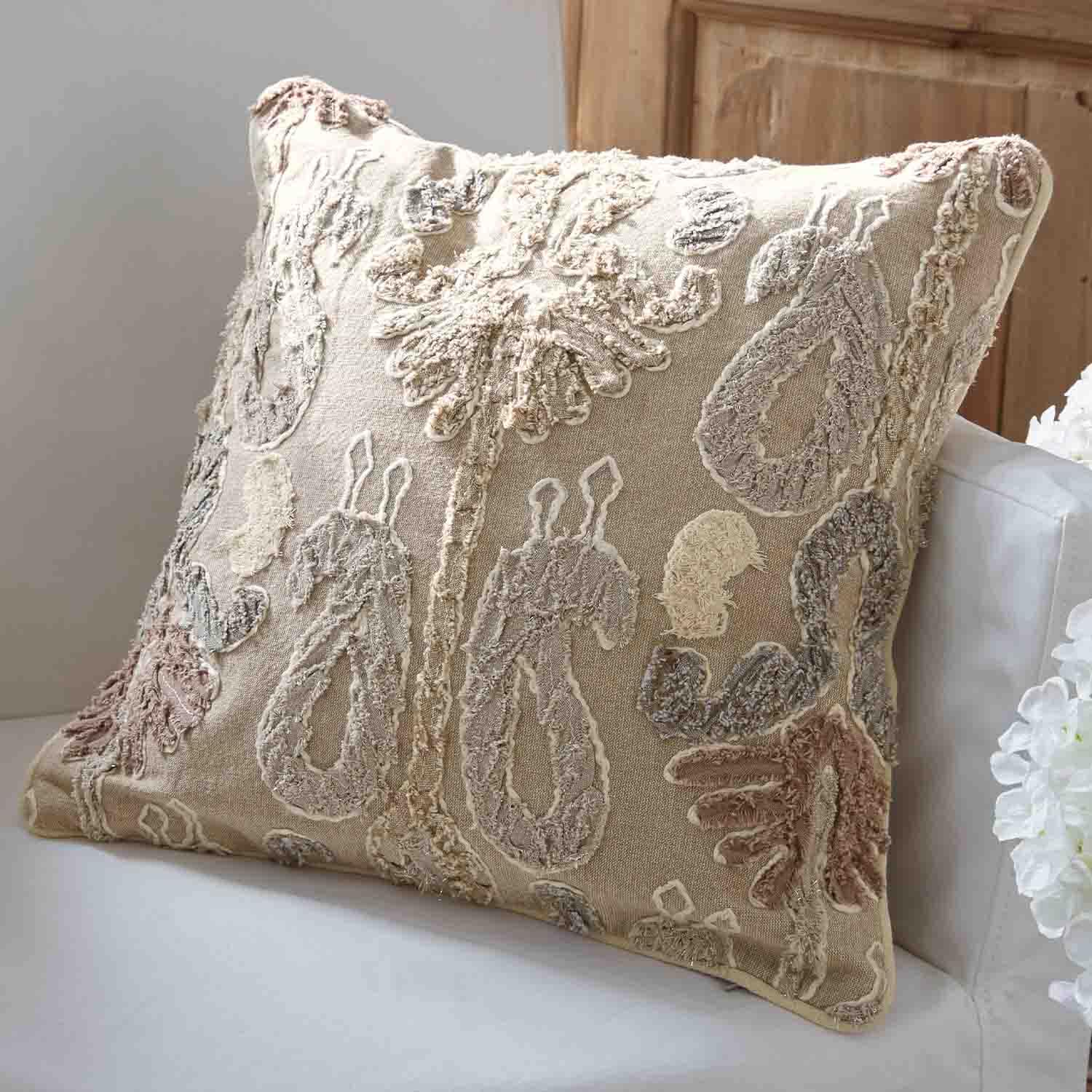 Cojín decorativo beige con bordado en colores pastel sobre sofá blanco para decoración