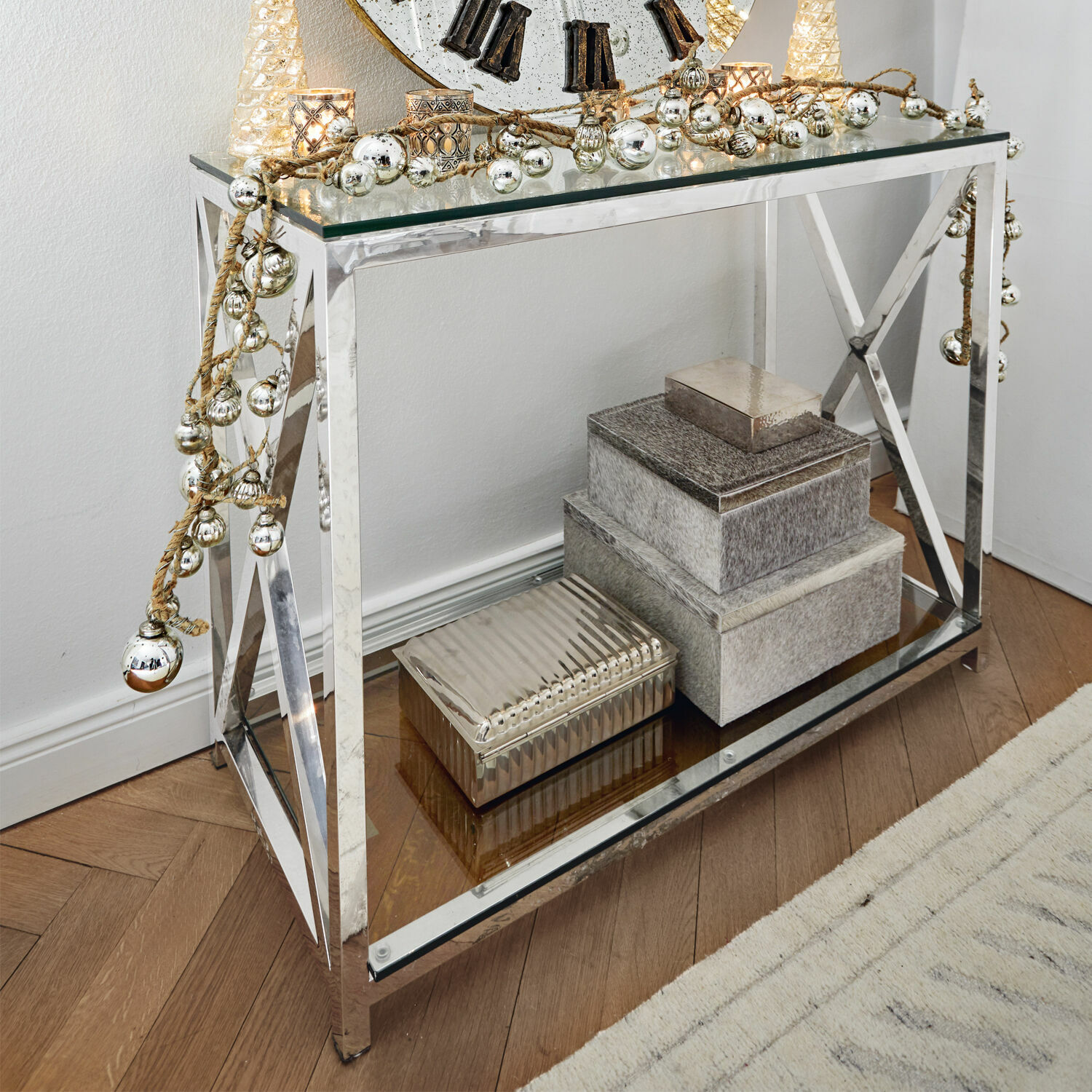 Mesa moderna con estructura metálica y superficie de vidrio, decorada con cajas y adornos navideños plateados