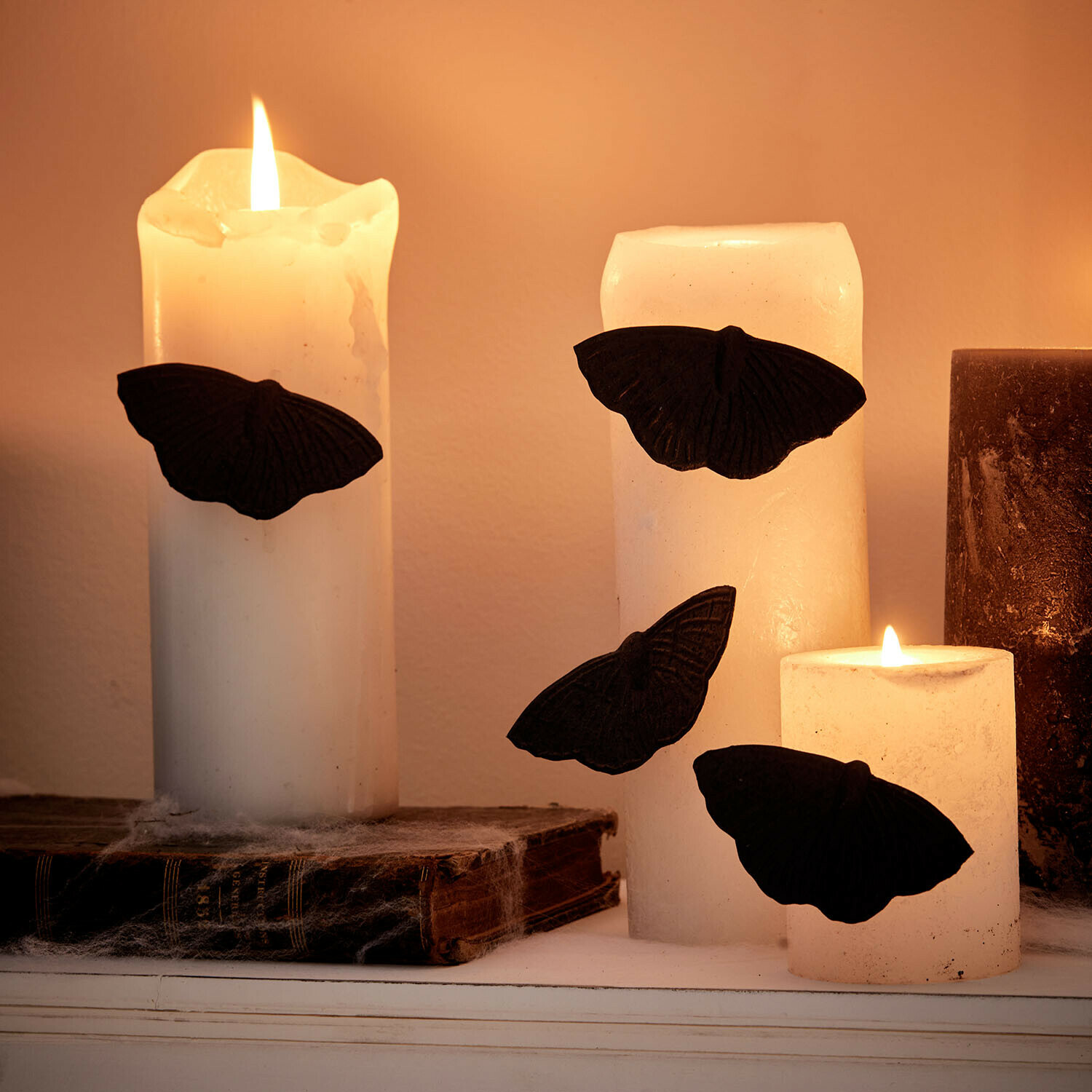 Set de 4 pines decorativos Orlenaith Velas blancas con mariposas negras decorativas sobre libros antiguos, iluminación ambiental cálida