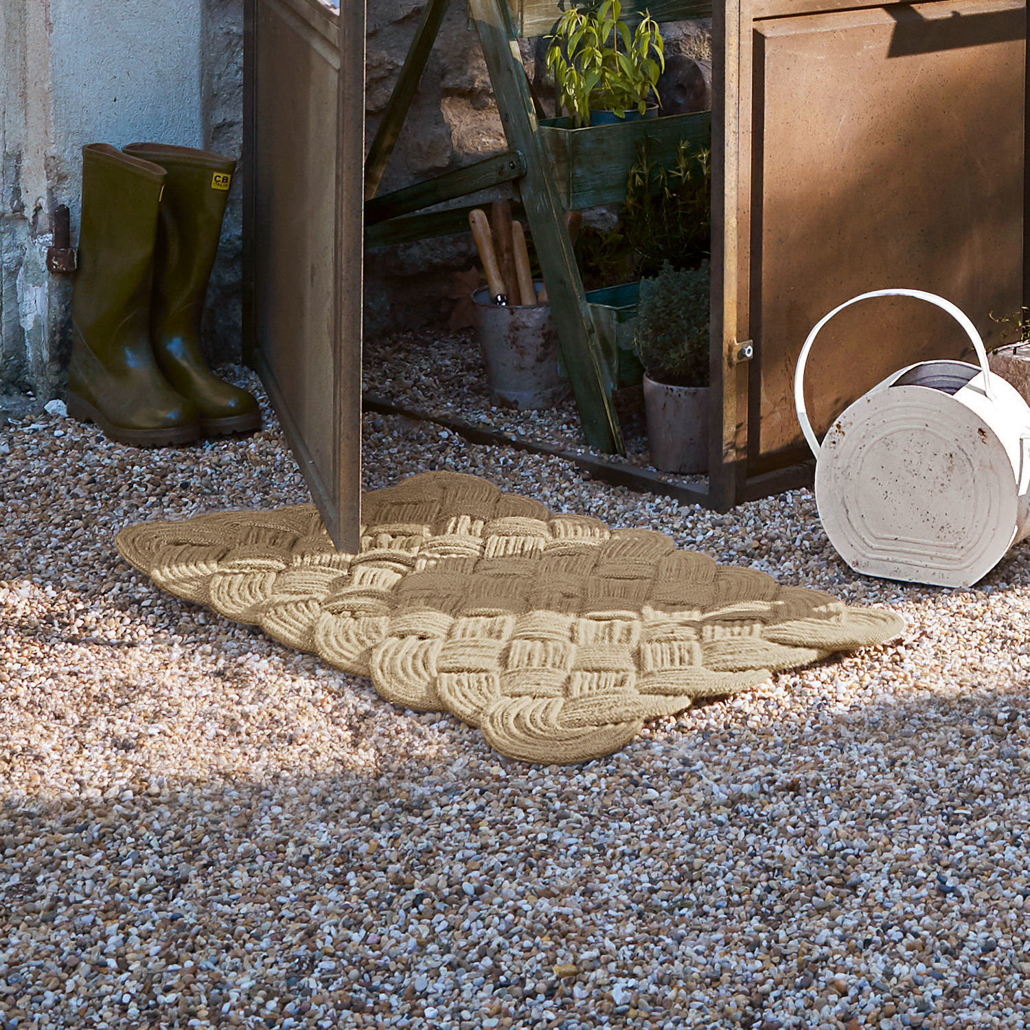 Felpudo Harman Felpudo beige tejido de material natural sobre grava frente a puerta de jardín abierta