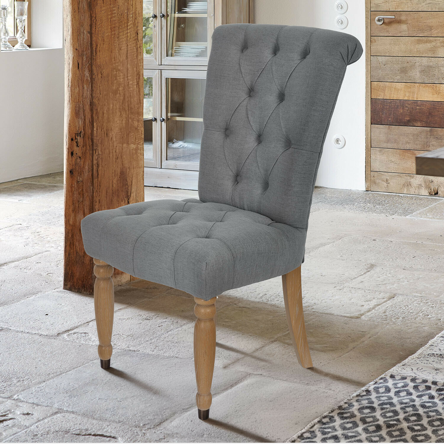 Silla tapizada gris con patas de madera en interior rústico con suelo de piedra