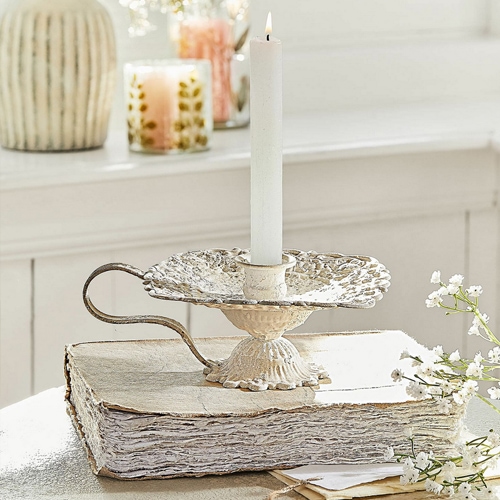Candelabro metálico vintage color crema sobre libro blanco, decoración de mesa con flores blancas