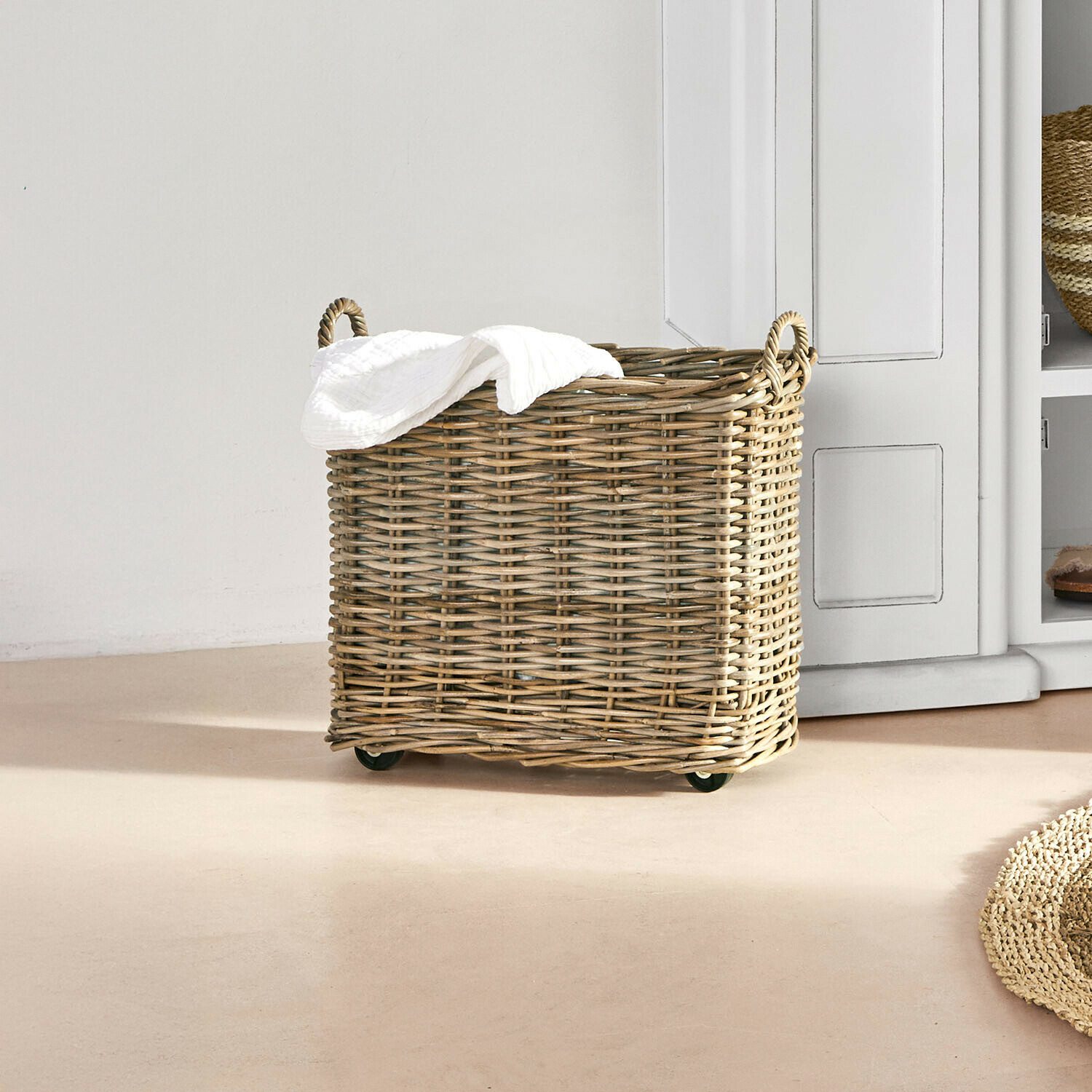 Cesto con ruedas Farivon Cesto de mimbre natural con ruedas y toalla blanca en interior luminoso y minimalista