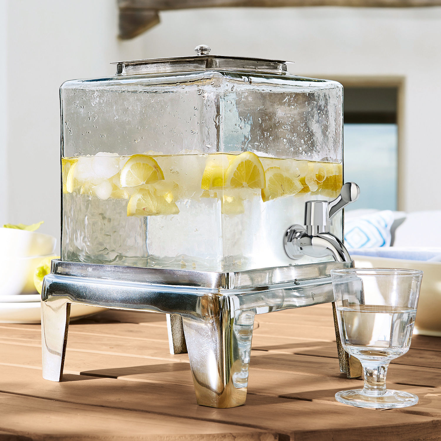 Dispensador de bebidas Osric Dispensador de bebidas de vidrio con base metálica y grifo, lleno de agua con limón
