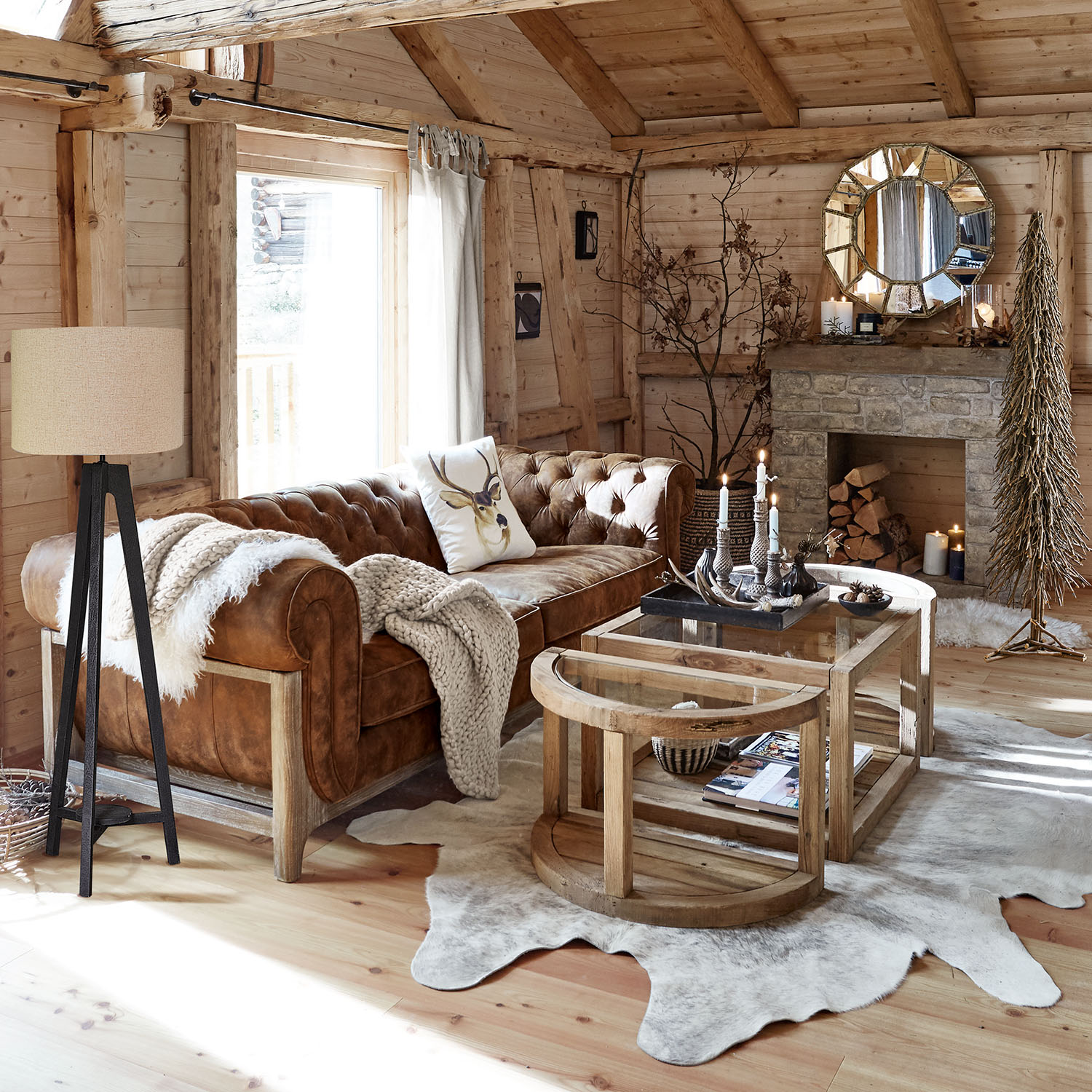 Salón acogedor con sofá de cuero marrón, mesas de madera y chimenea rústica de piedra