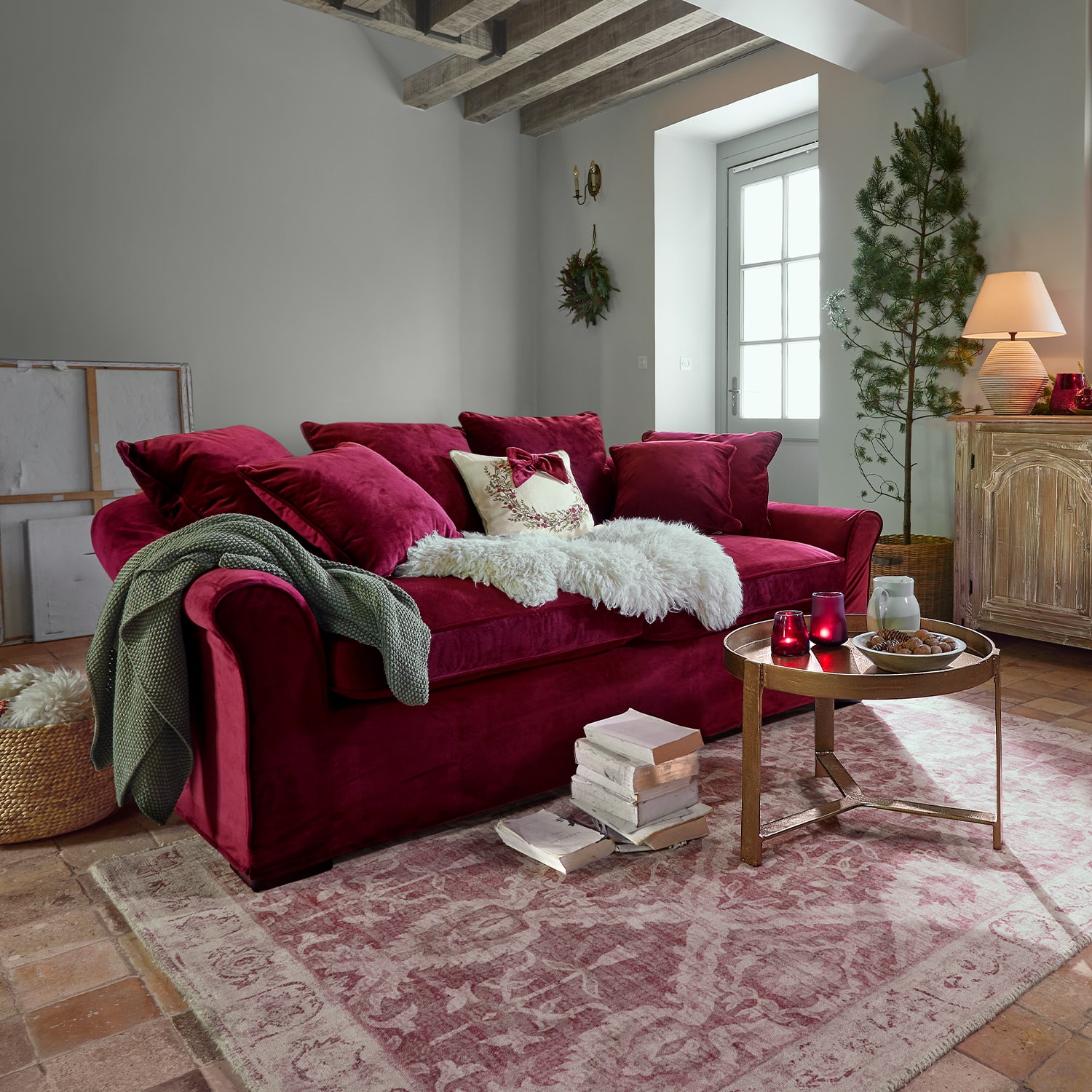 Sofá rojo de terciopelo con cojines y manta suave en sala acogedora con escalera de madera