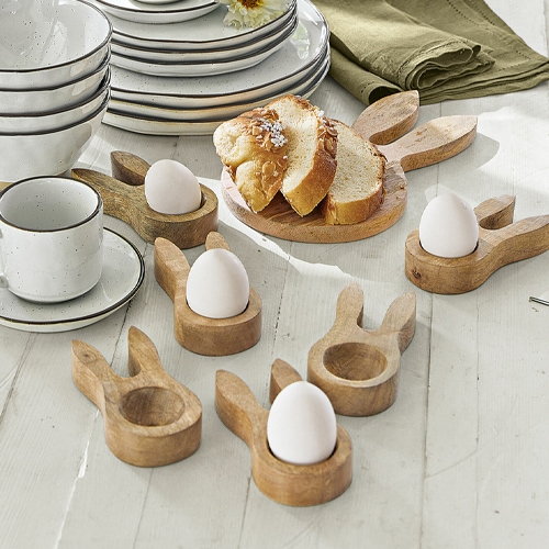 Soportes de huevos de madera con forma de orejas de conejo sobre mesa blanca con pan y vajilla