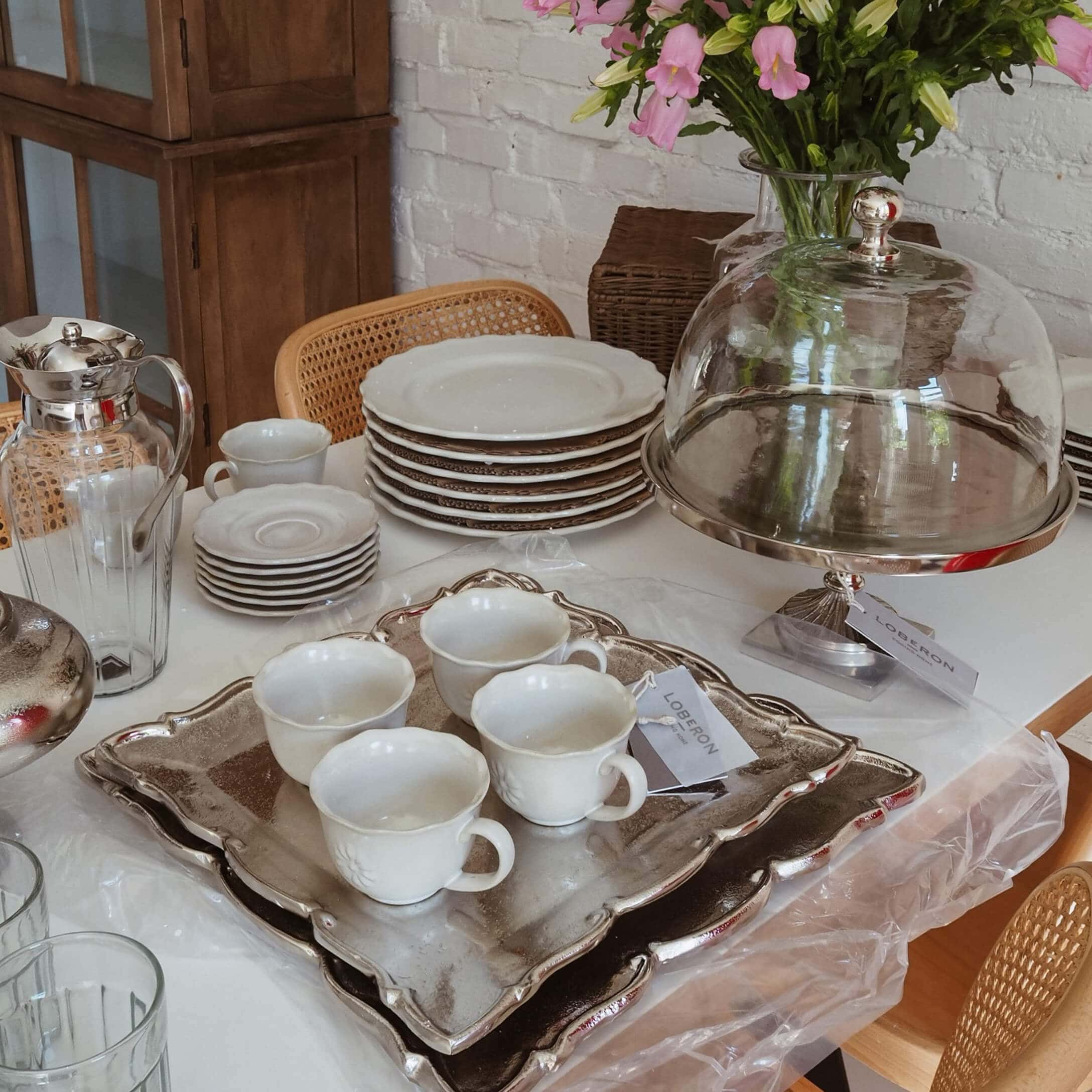 Juego de porcelana blanca con tazas y platos sobre bandeja plateada, decoración de mesa slow living