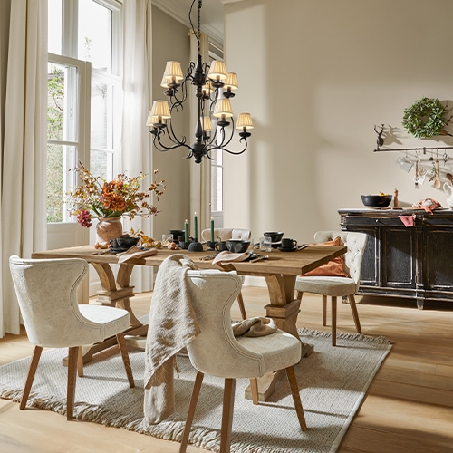 Comedor con mesa de madera, sillas tapizadas crema, decoración floral y lámpara de araña negra