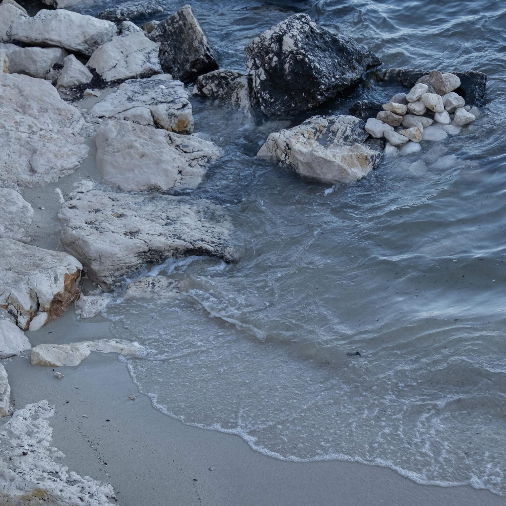 Orilla del mar con rocas claras y oscuras y olas rompiendo sobre la arena
