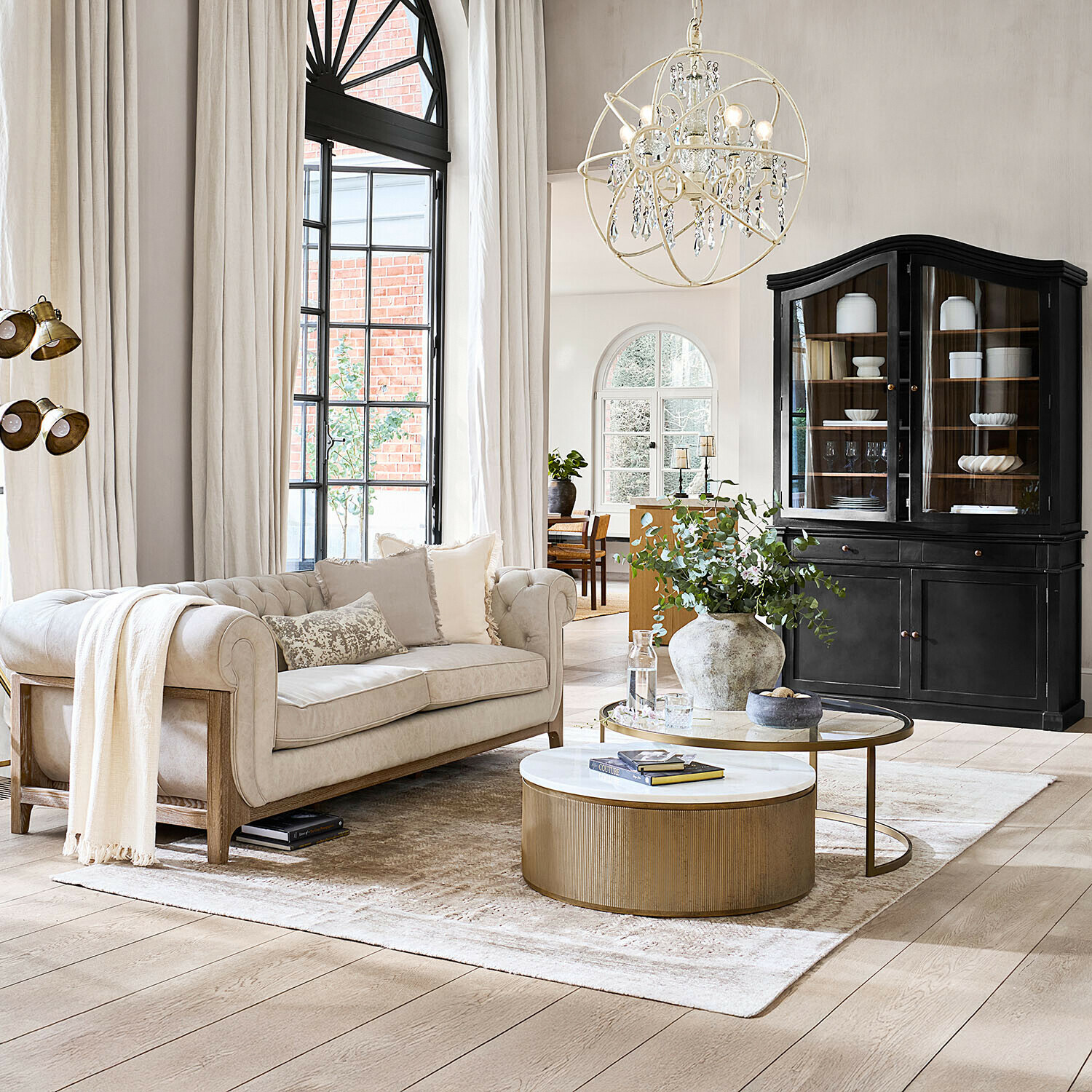 Alfombra Ashmere Sofá beige con marco de madera y cojines en salón luminoso con vitrina negra y mesa de centro dorada