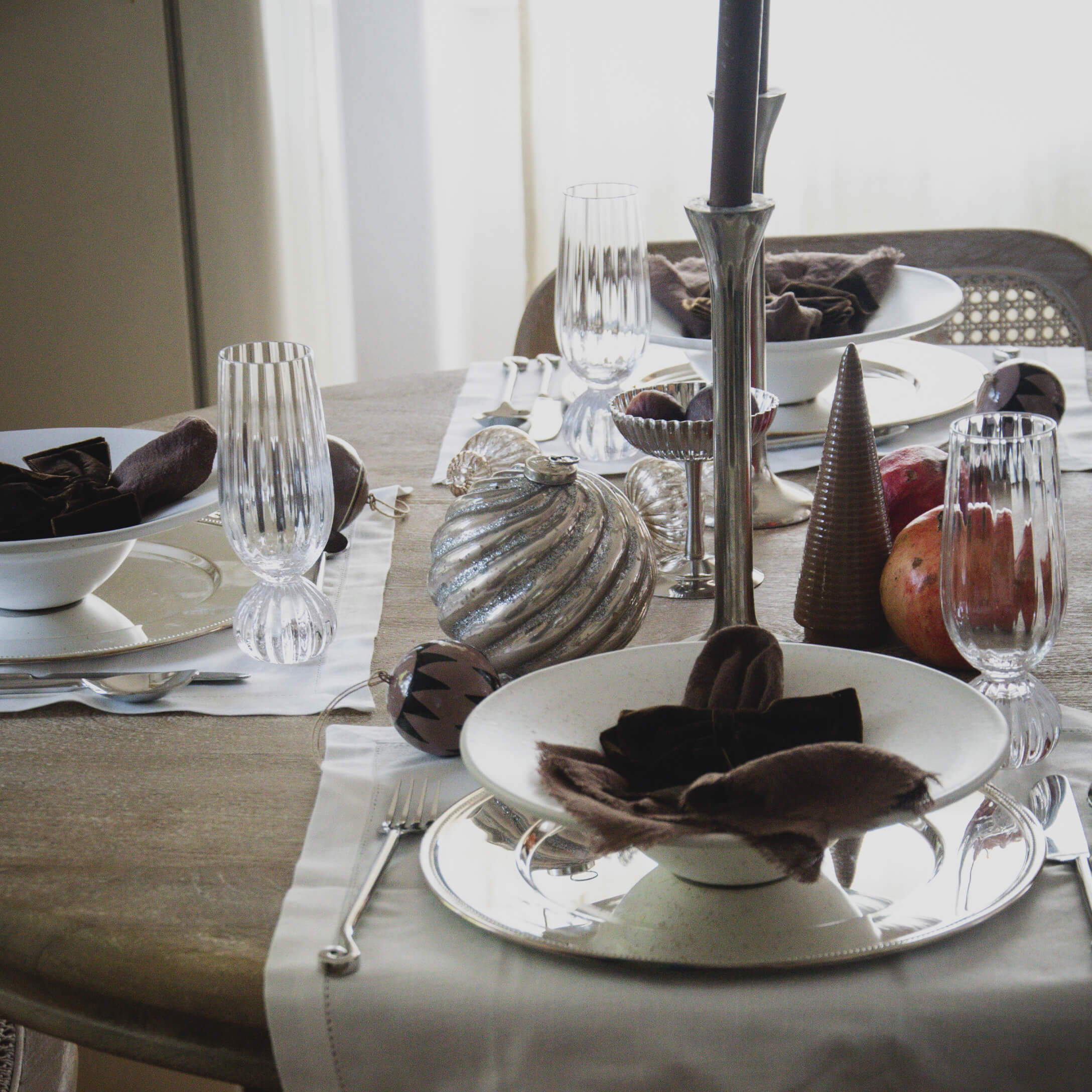 Mesa elegantemente puesta con vajilla blanca, copas de cristal y decoraciones naturales para comida formal