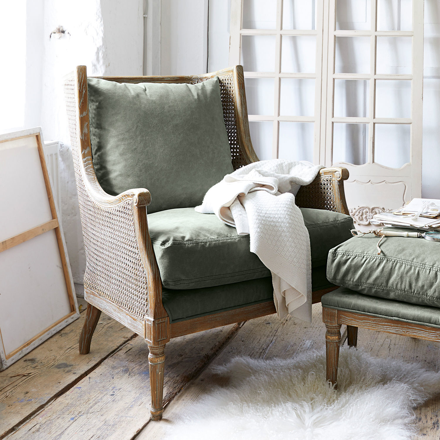 Sillón Greenbrier Sillón con estructura de madera y tapizado verde, manta blanca sobre alfombra de piel clara