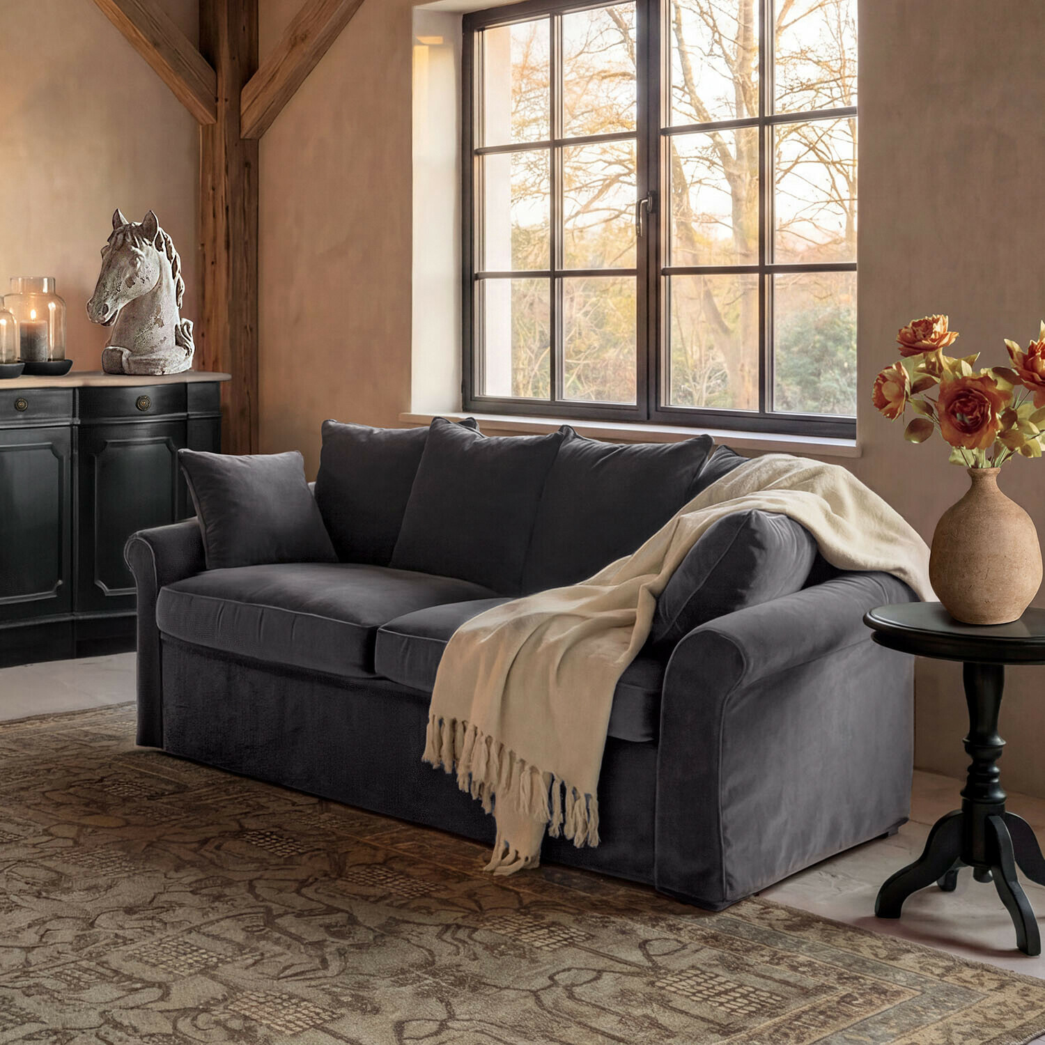Sofá Long Beach Sofá de terciopelo gris con manta crema en salón acogedor con decoración de cabeza de caballo y flores