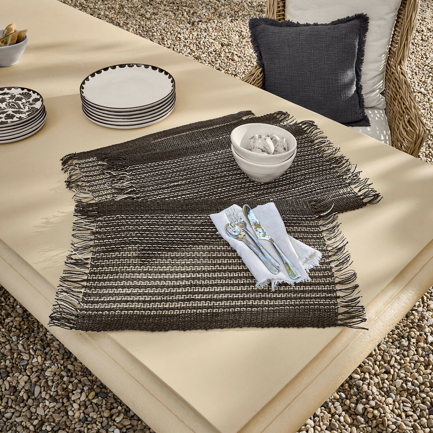 Set de 4 manteles individuales Tarevo Individuales tejidos marrones con flecos sobre mesa beige con vajilla y cubiertos