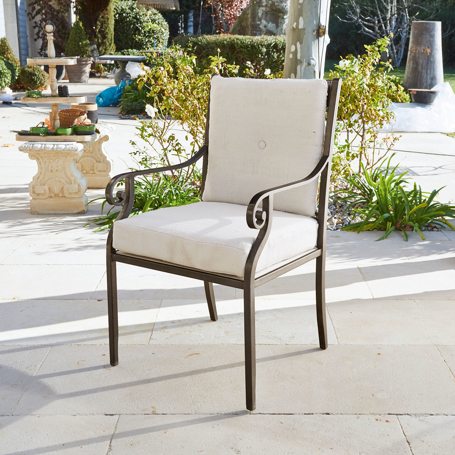 Silla de jardín con estructura metálica y cojín crema en terraza de piedra clara